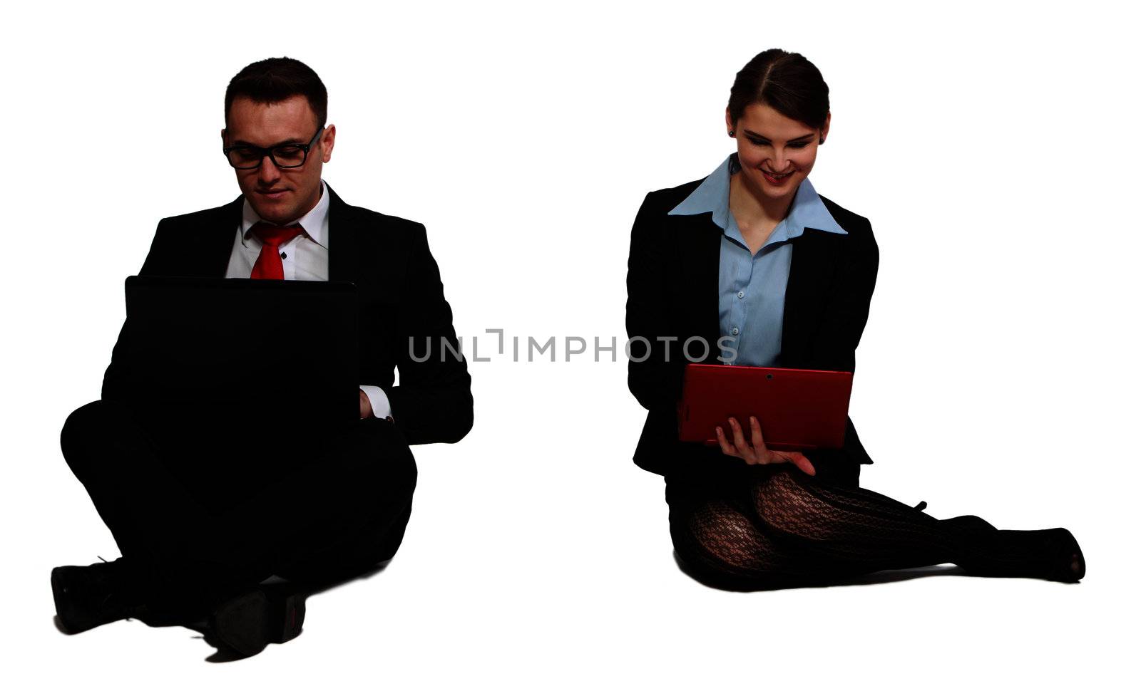 Young business couple working on laptops while sitting against a white background.