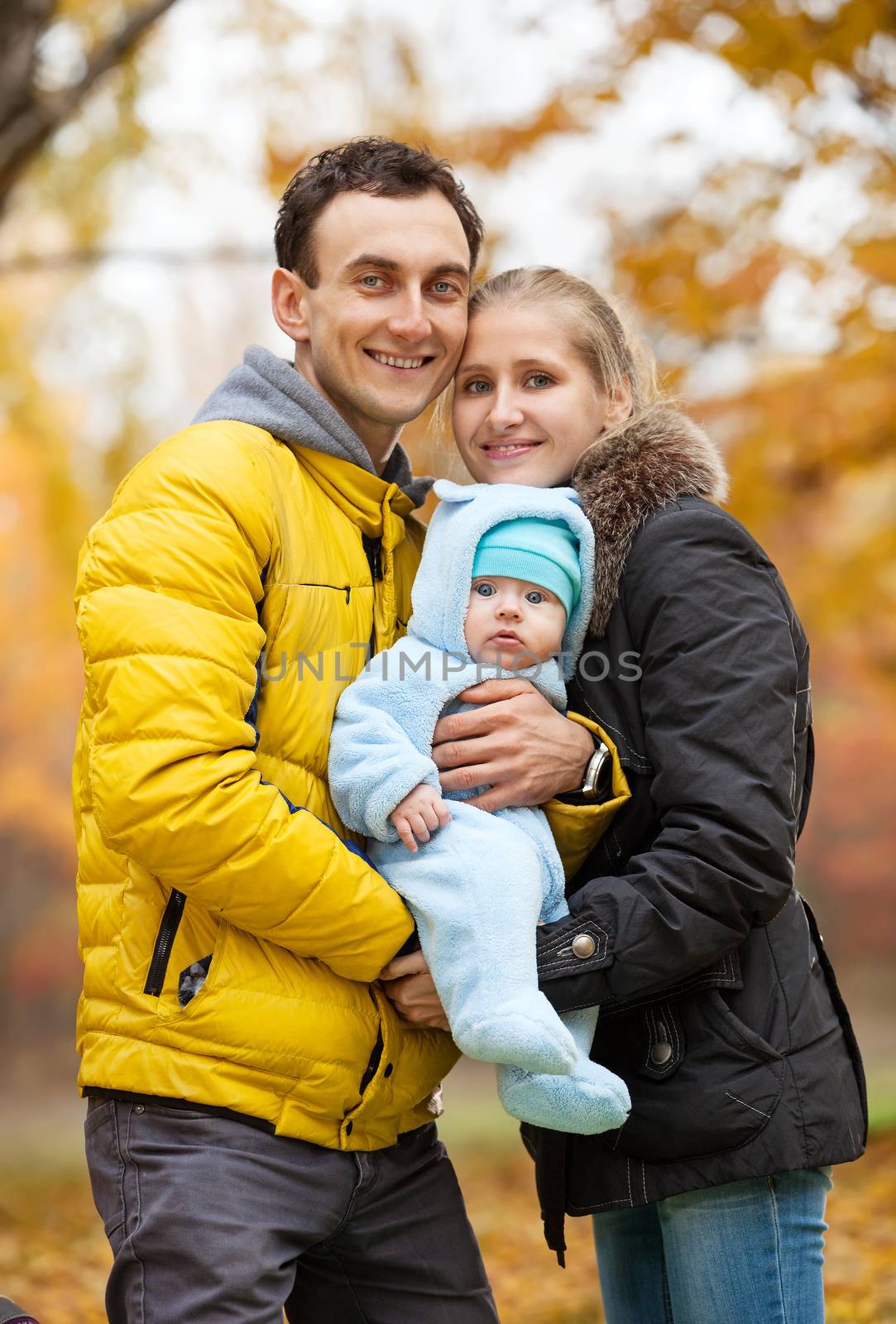 Young couple with baby boy on looking at camera in autumn park