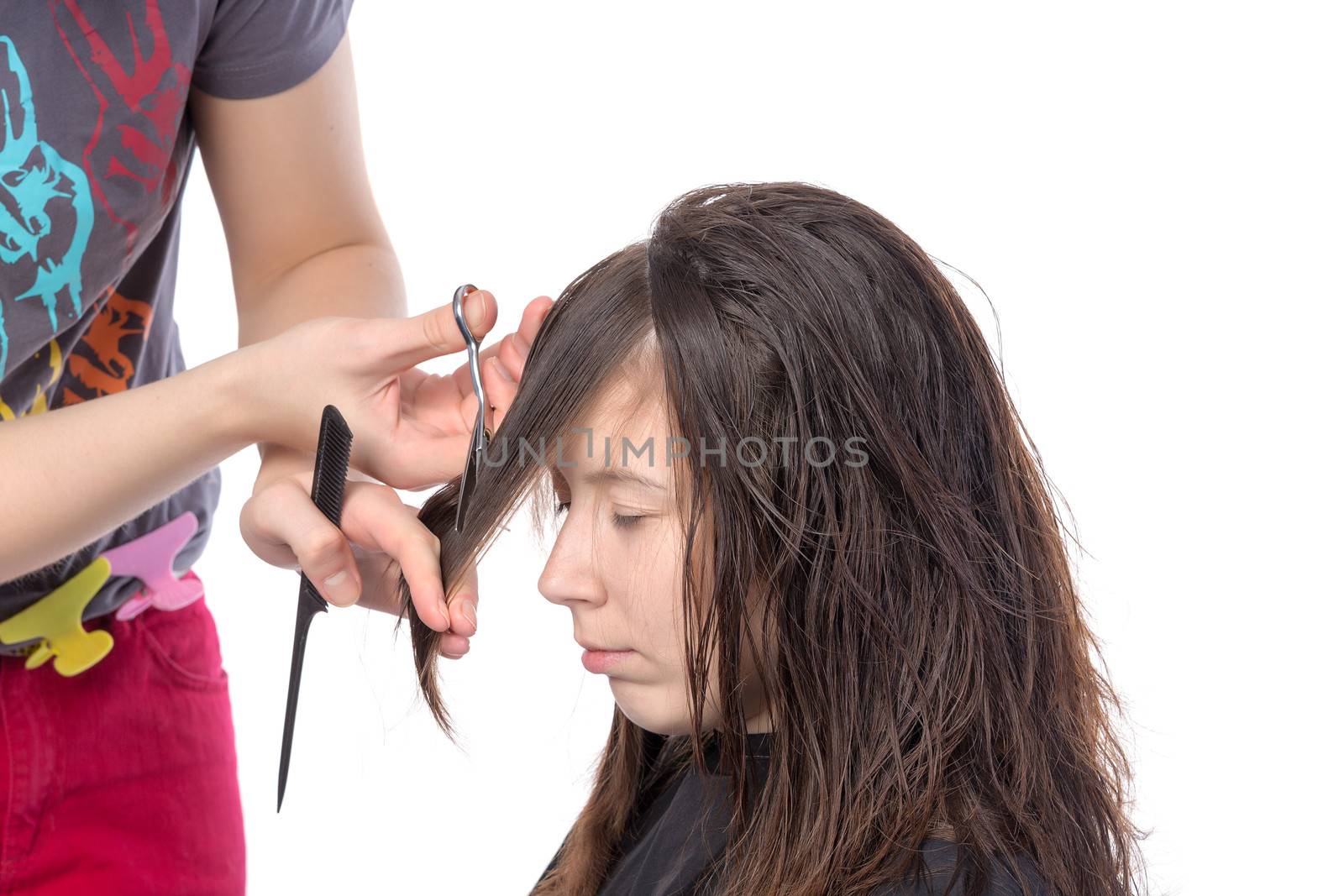 Young woman having a hair cut with a hairdresser trimming her fringe on her long brunette hair, isolated on white