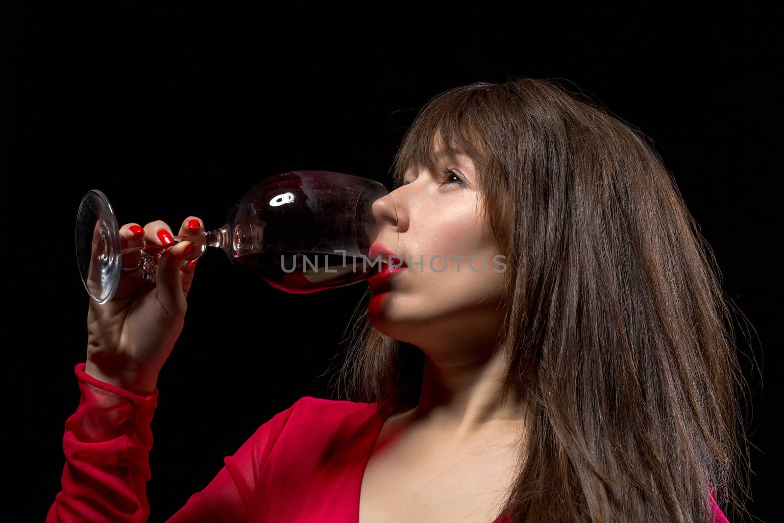 Young woman drinking red wine from a wineglass against a dark background