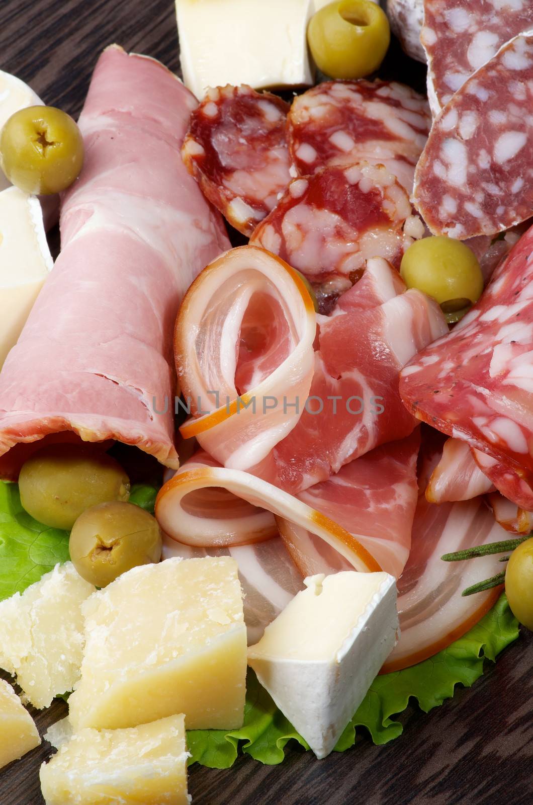 Heap of Delicatessen Cold Cuts with Smoked Ham, Pepperoni, Salami, Finocchiona, and Various Cheese with Grana Padano, Camembert and Brie  closeup on Dark Wooden background