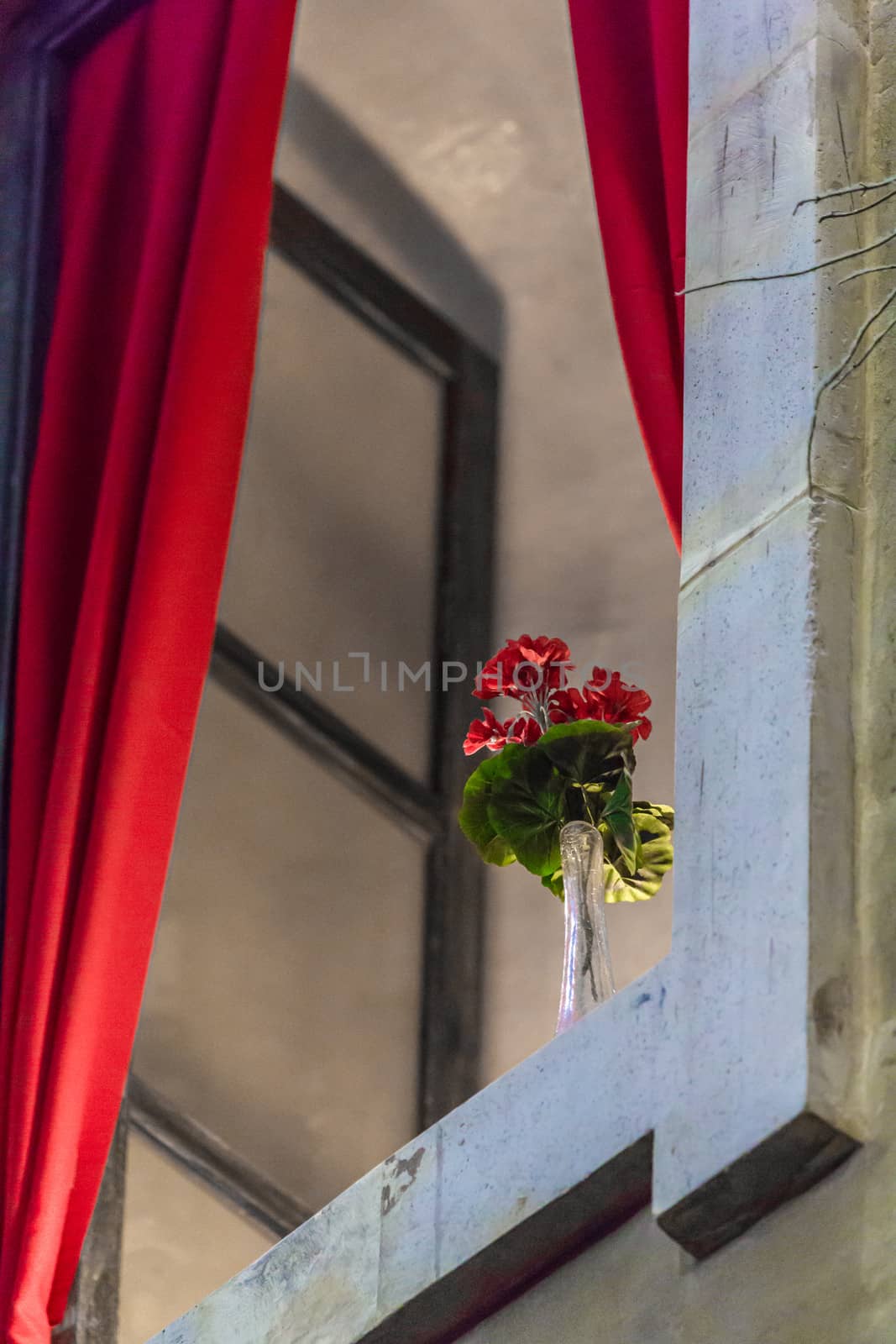 A red flower placed on an open window ledge with a red curtain