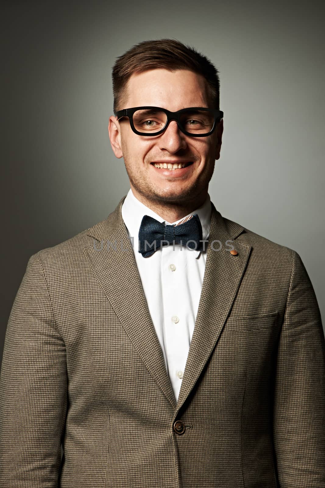 Confident nerd in eyeglasses and bow tie against grey background