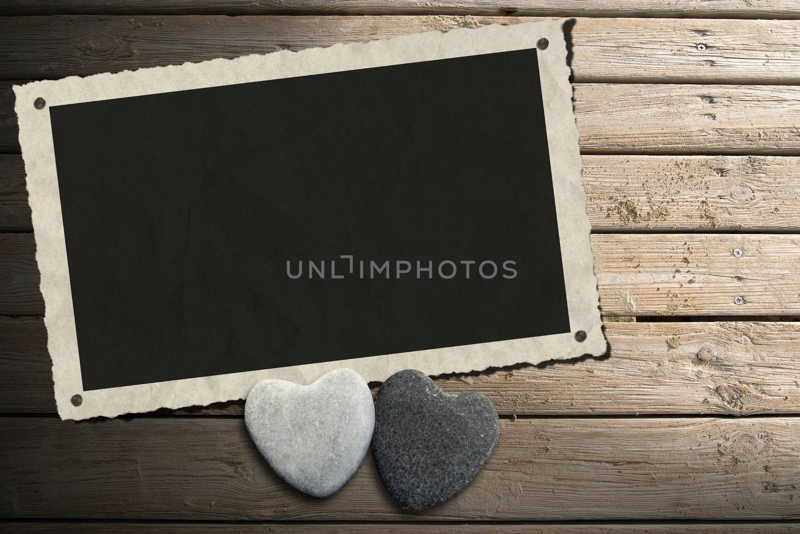Aged and romantic photo frame with two stone hearts on wooden floor with sand