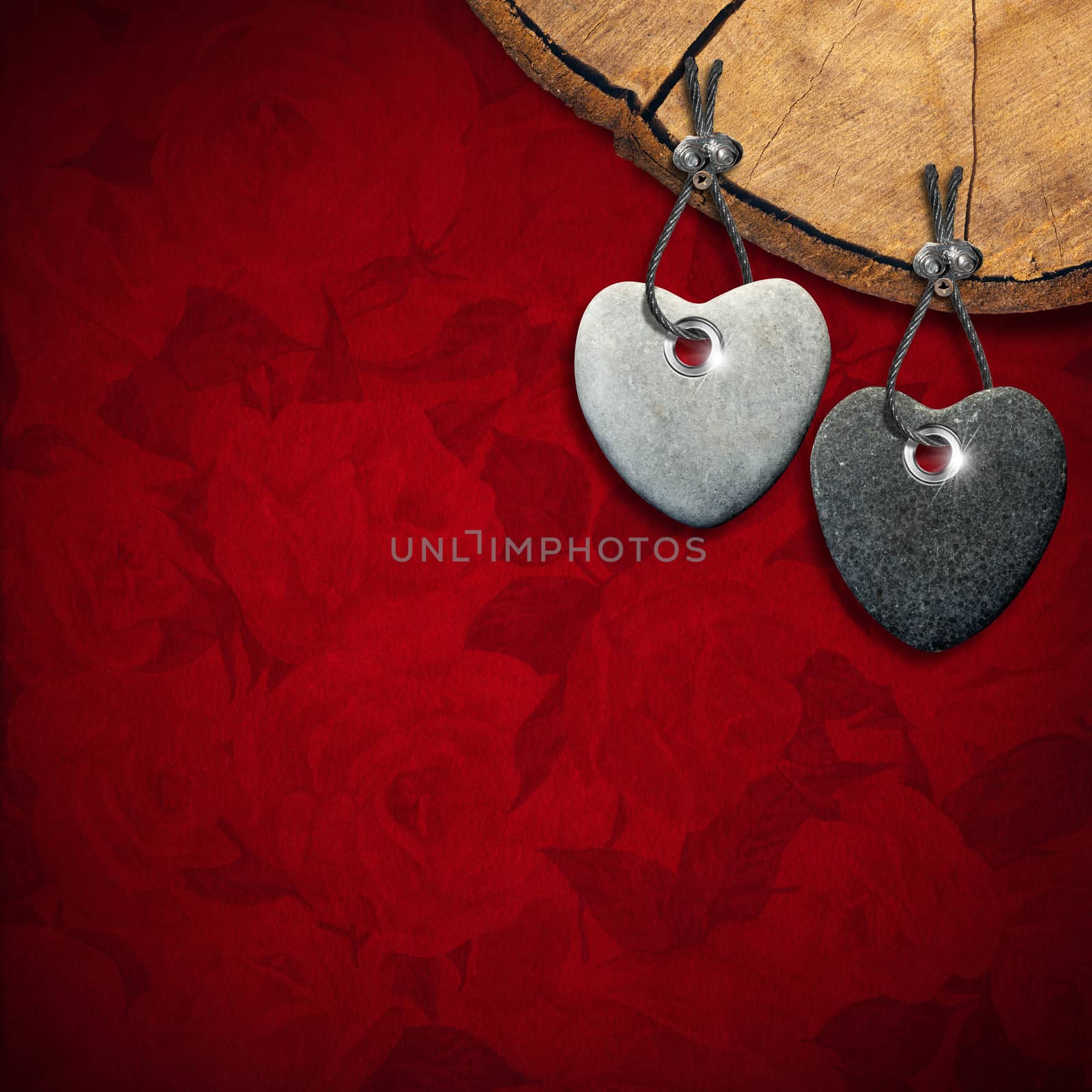 Two stone hearts hanging from a section of tree trunk on red velvet background with roses flowers