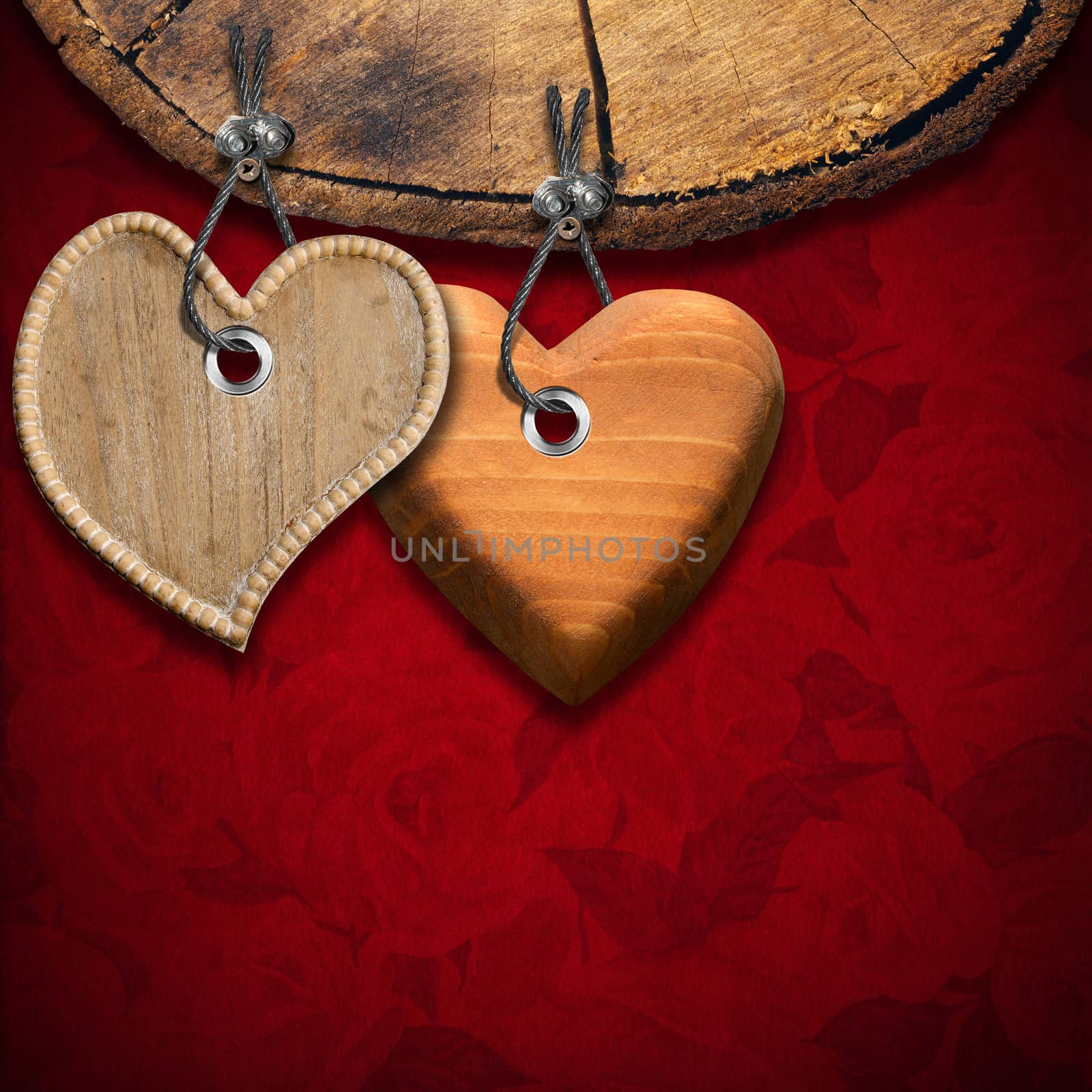 Two wooden hearts hanging from a section of tree trunk on red velvet background with roses flowers