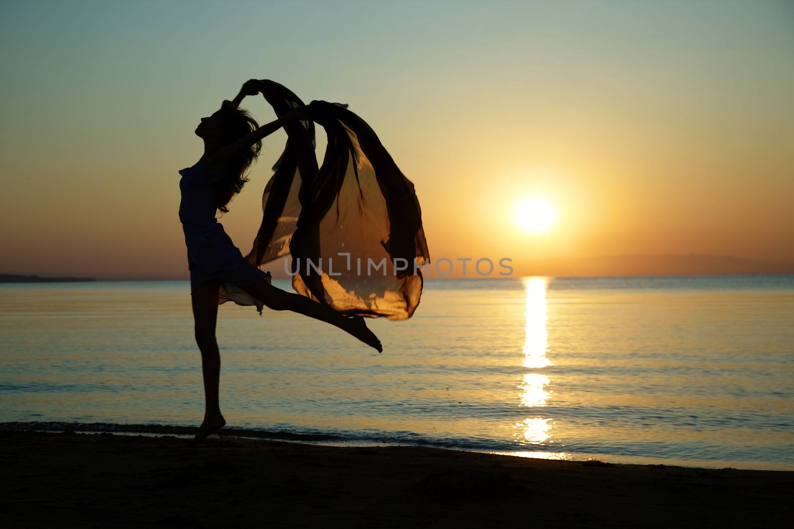 Silouette of the nifty woman dancing at the sea during sunset. Natural light and darkness. Artistic colors added