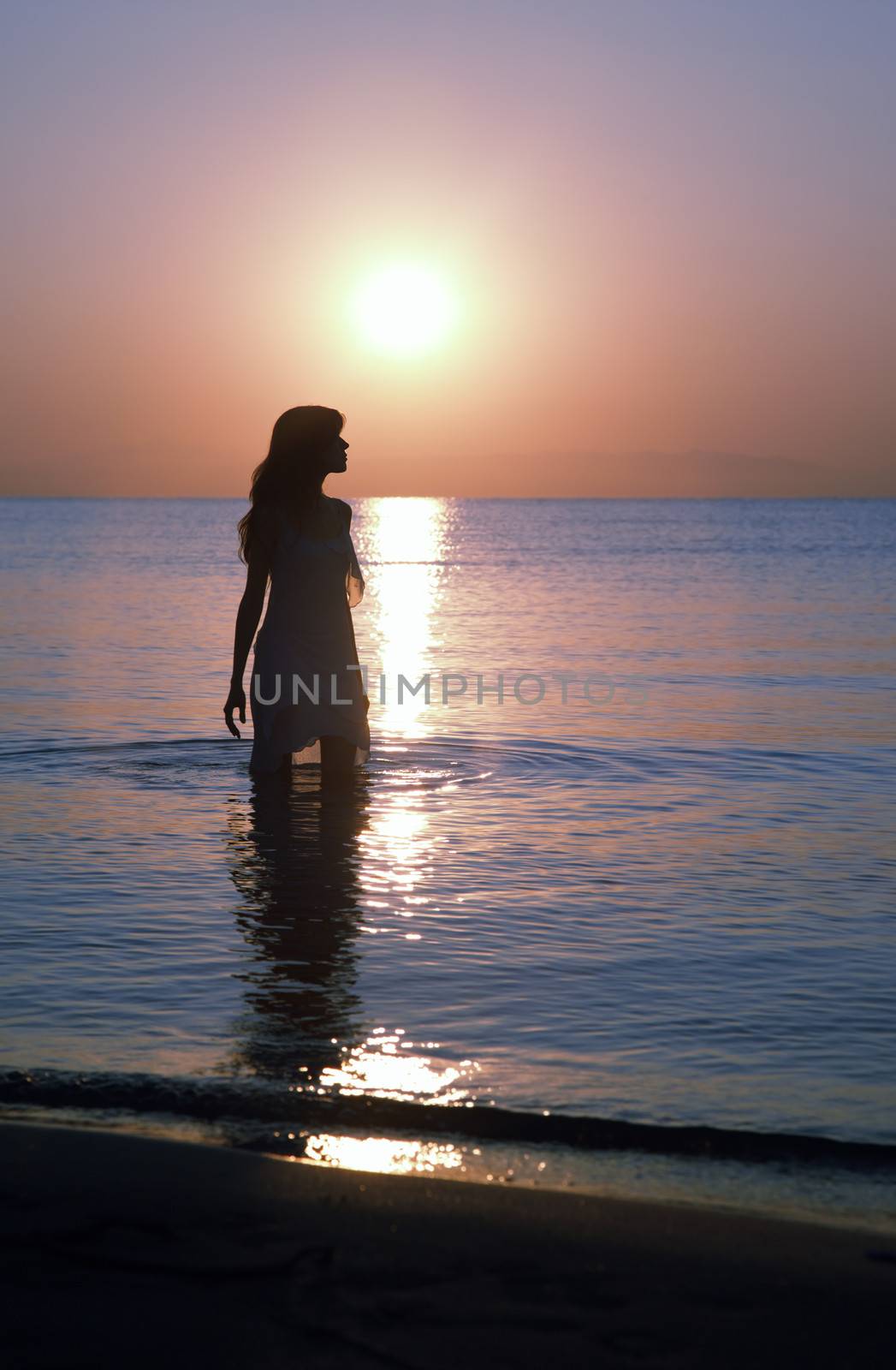 Silhouette of happy woman standing in the water at the beach during twilight