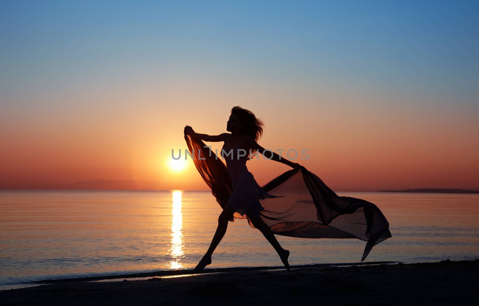 Silhouette of the happy woman with fiber dancing and jumping at the sunset beach