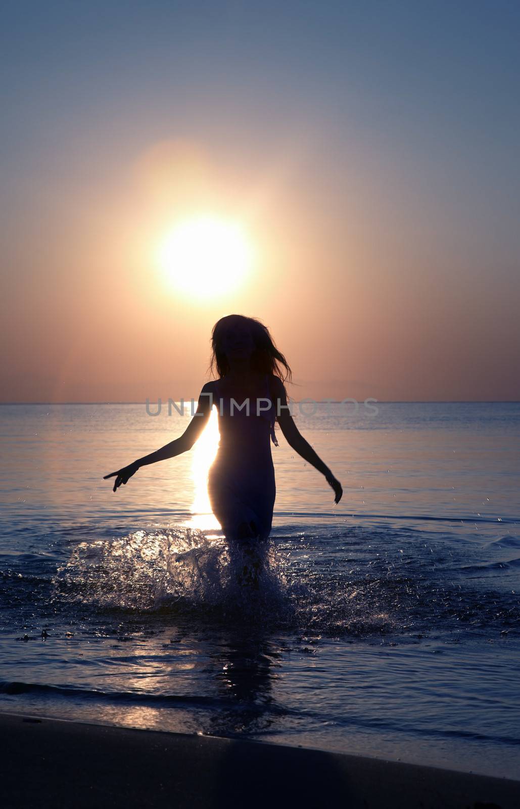 Silhouette of the woman running in the water during sunset. Natural light and colors