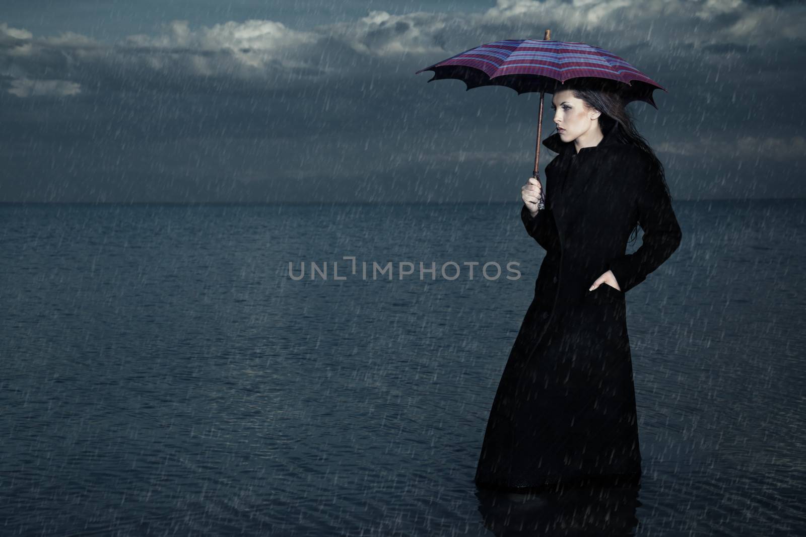 Lady with umbrella standing under the rain in the sea