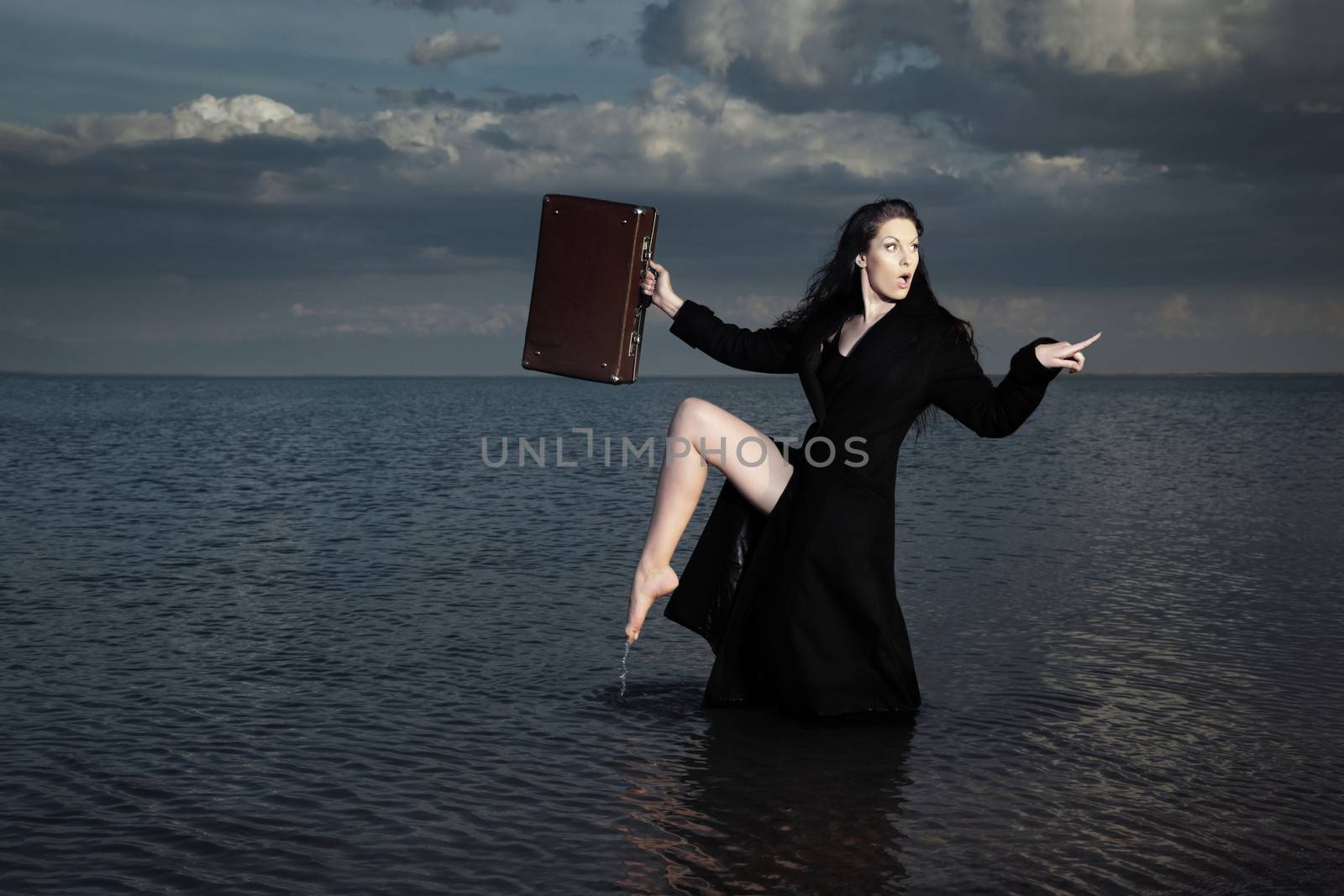 Stylish lady in the black coat with case standing in the dark water
