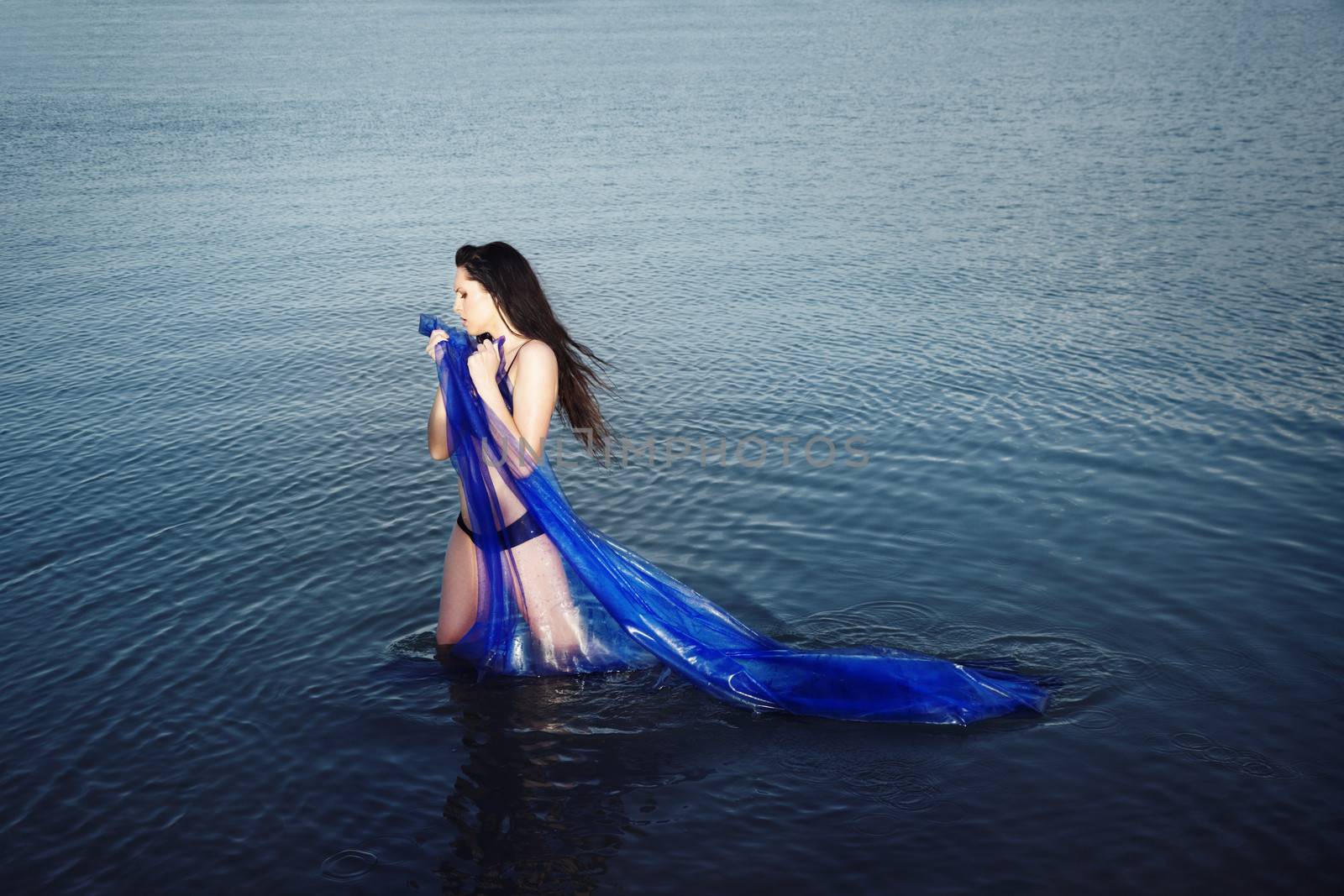 Sensual lady with blue fabric standing in the water