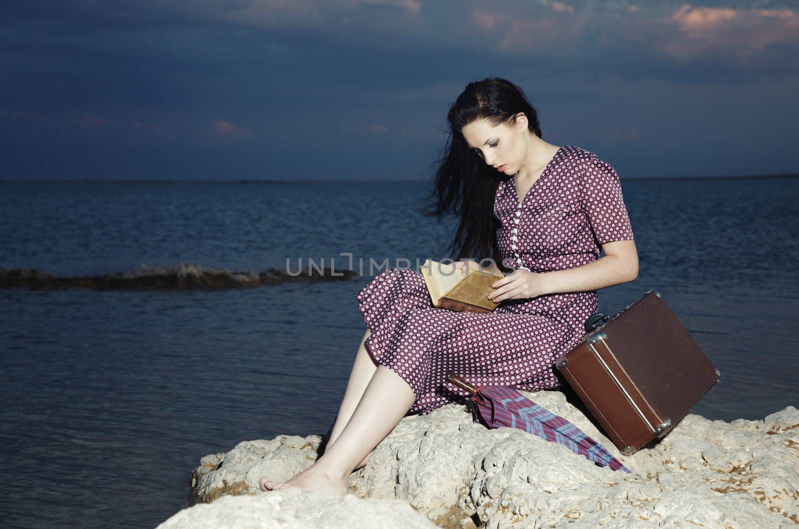 Single lady reading book outdoors at the ocean during sunset