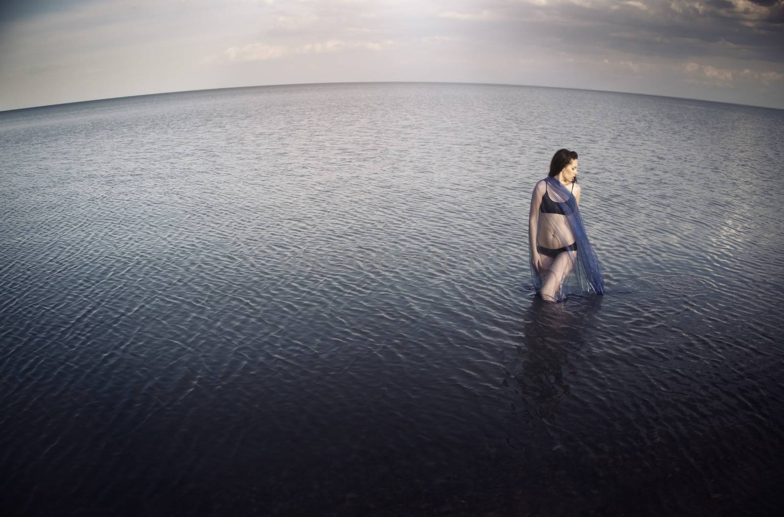 Woman in the sea before the storm. Horizontal photo. Artistic horizon distortion added due to the wide angle lens