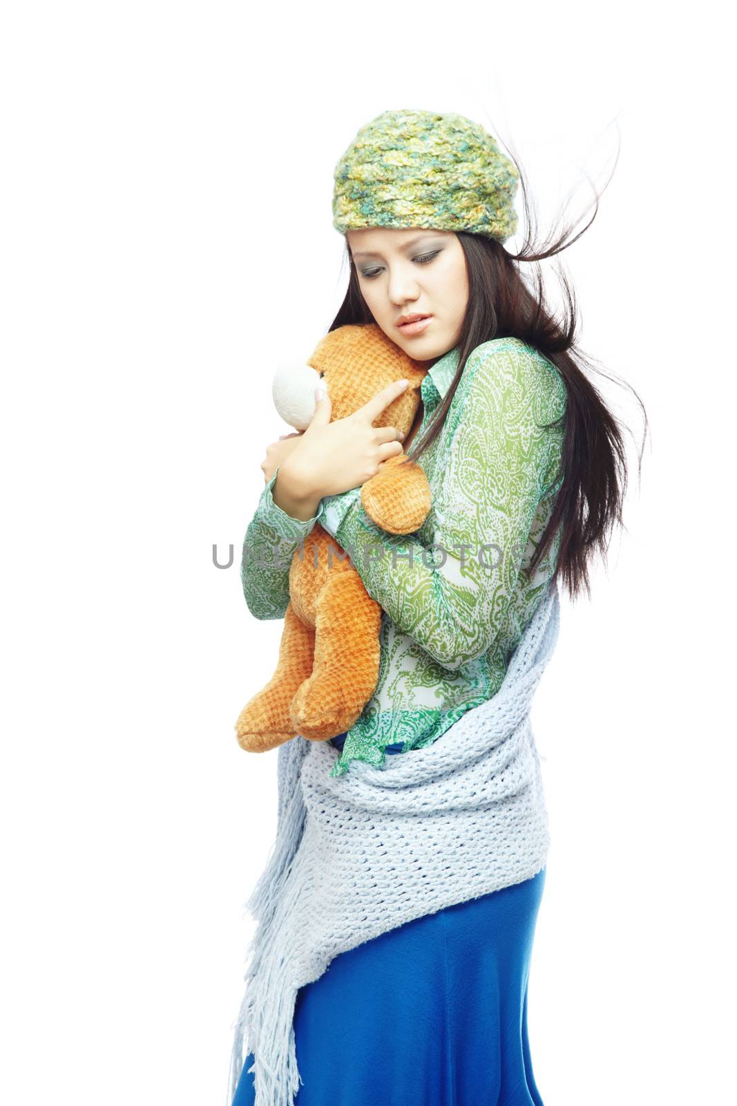 Sad young lady with blown hairs in the stylish clothes embracing Teddy bear on a white background 