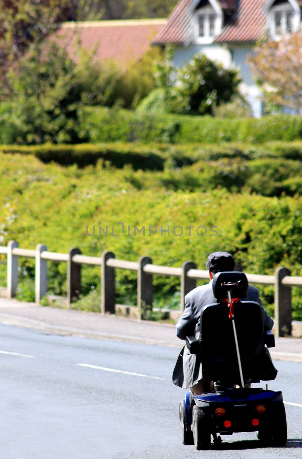 Rear view or senior man riding mobility scooter on countryside road.
