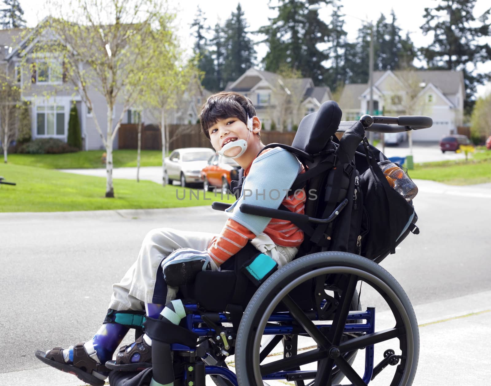 Happy disabled six year old boy waiting on sidewalk in wheelchair. Child has cerebral palsy