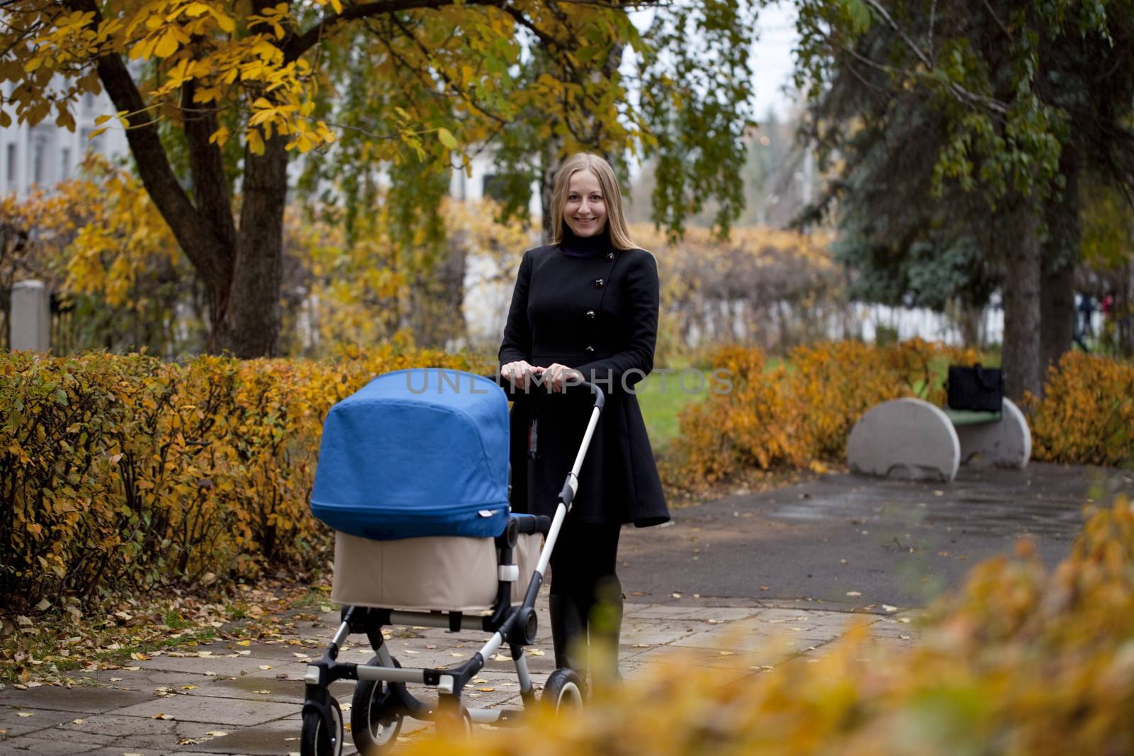 Mother with baby stroller for a newborn in autumn park