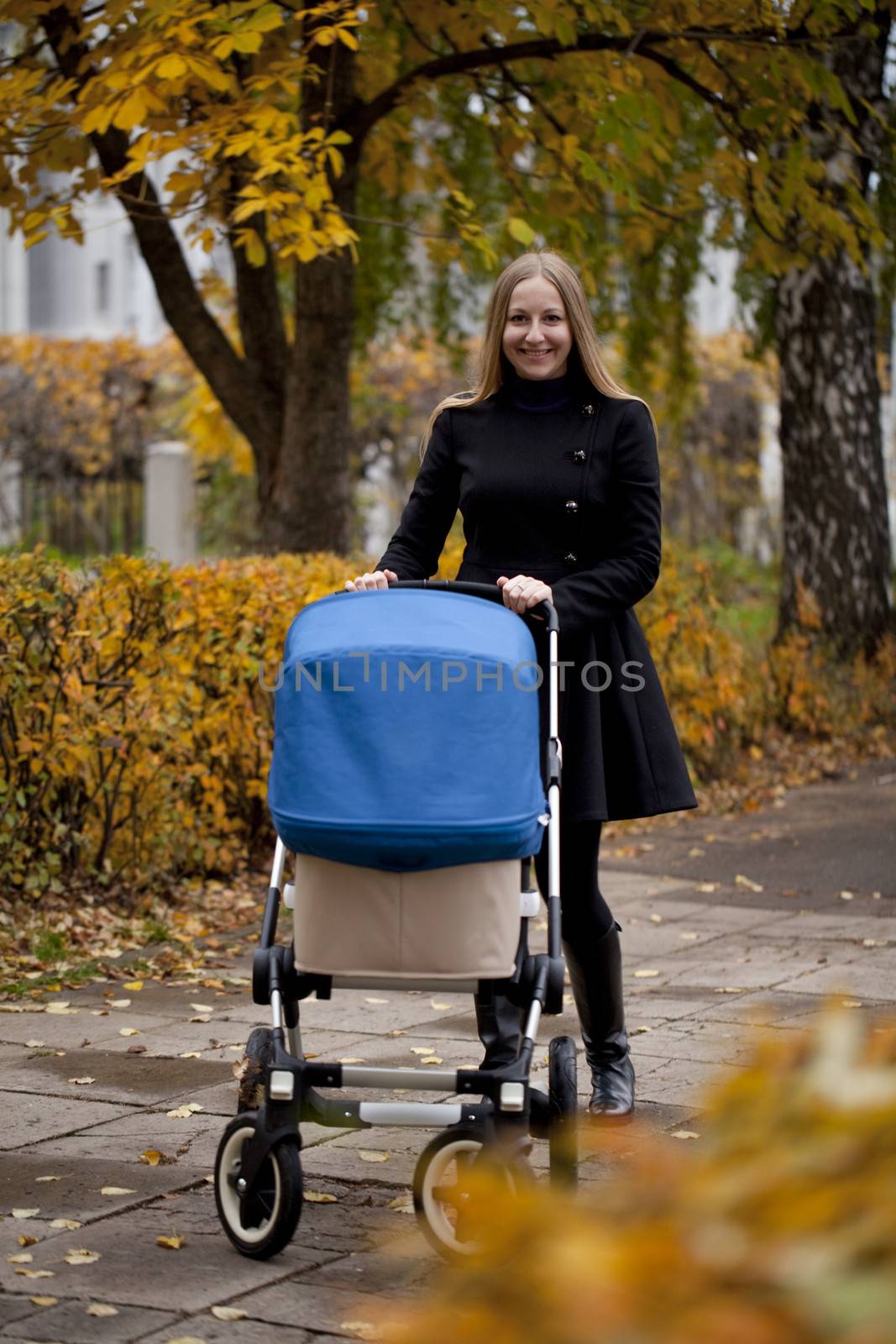 Mother with baby stroller for a newborn in autumn park