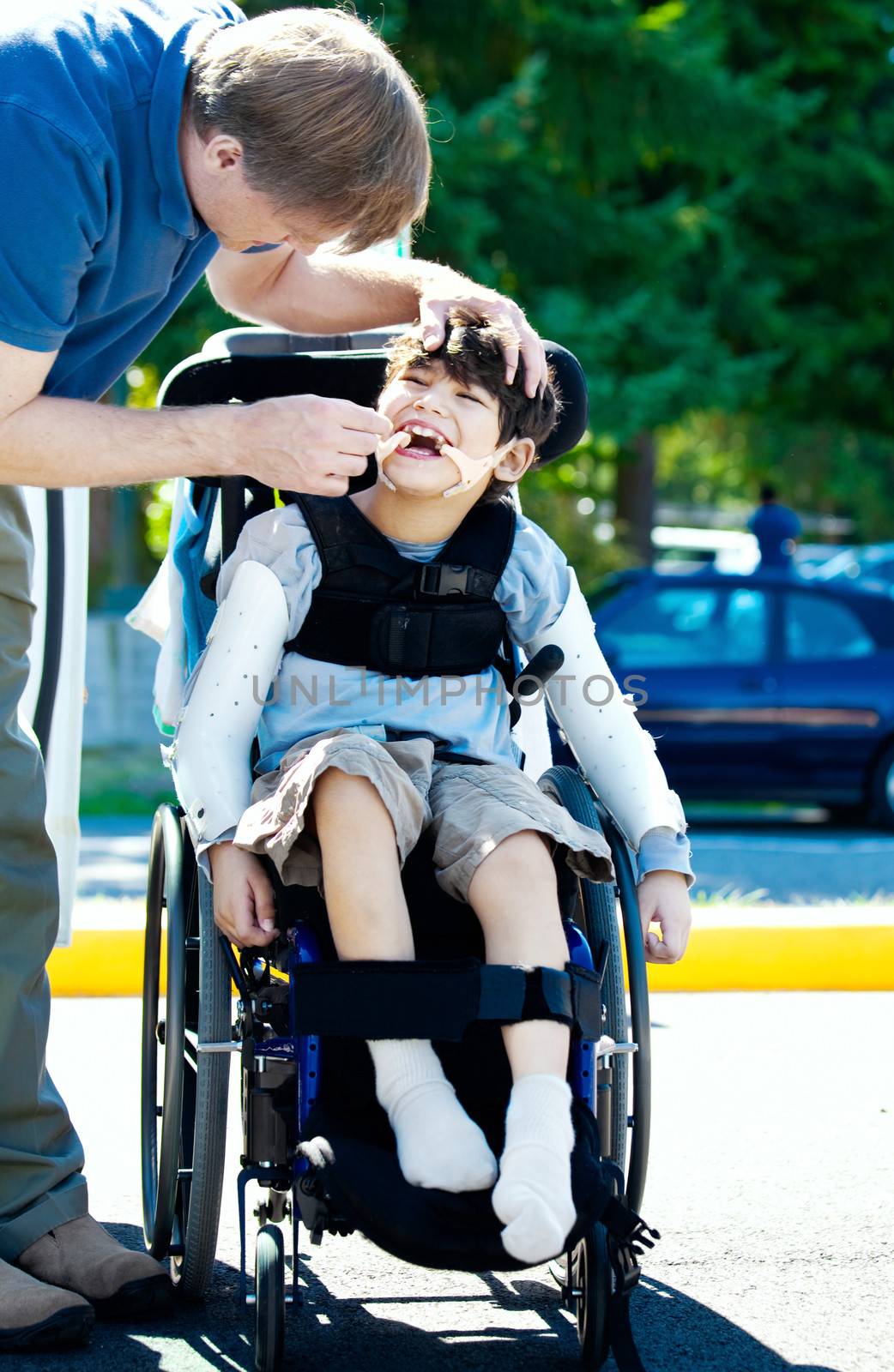 Father helping disabled child in wheelchair. Child has cerebral palsy.