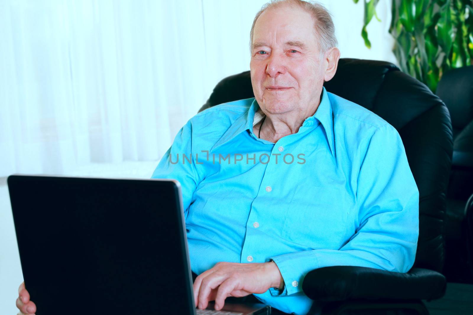 Elderly man using laptop computer sitting in leather recliner
