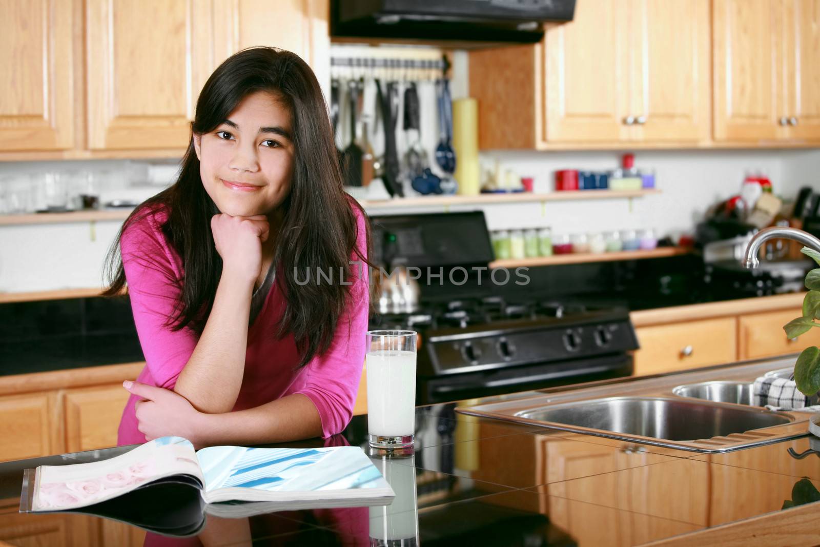 Teen girl relaxing in kitchen with magazine and glass of milk