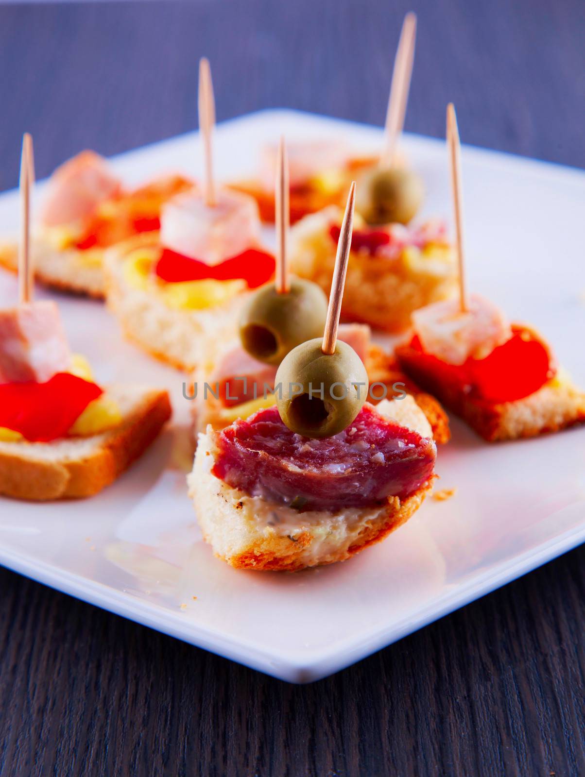 Appetizers with olives, sausage and tomatoes over white plate