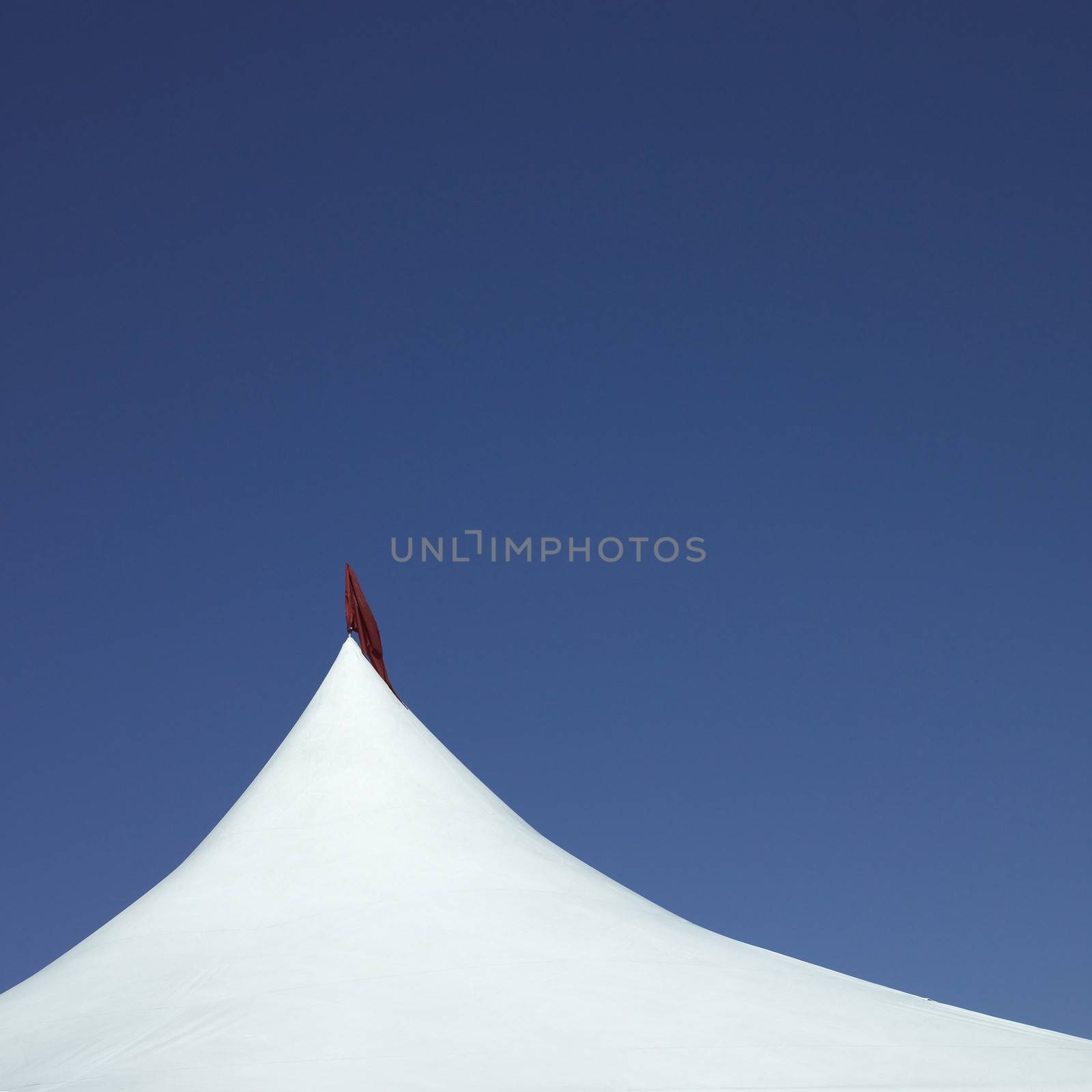 White tent with red flag against blue sky