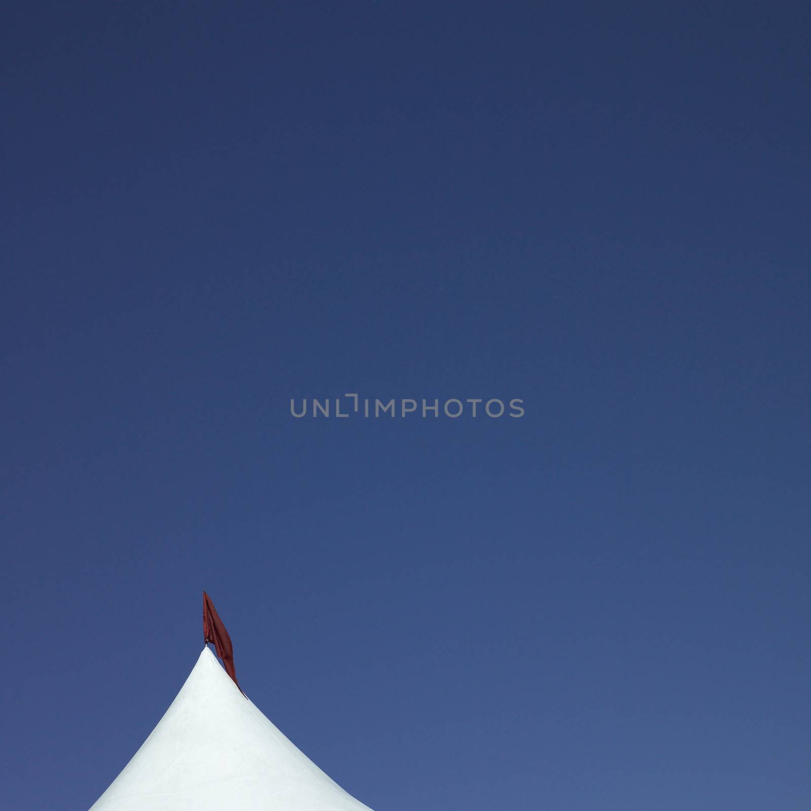 White tent with red flag against blue sky
