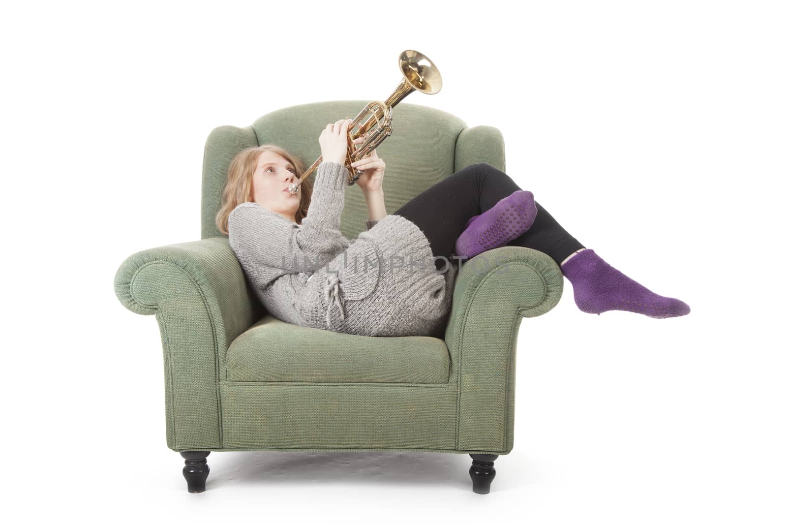 young pretty woman playing the trumpet in an armchair against white background