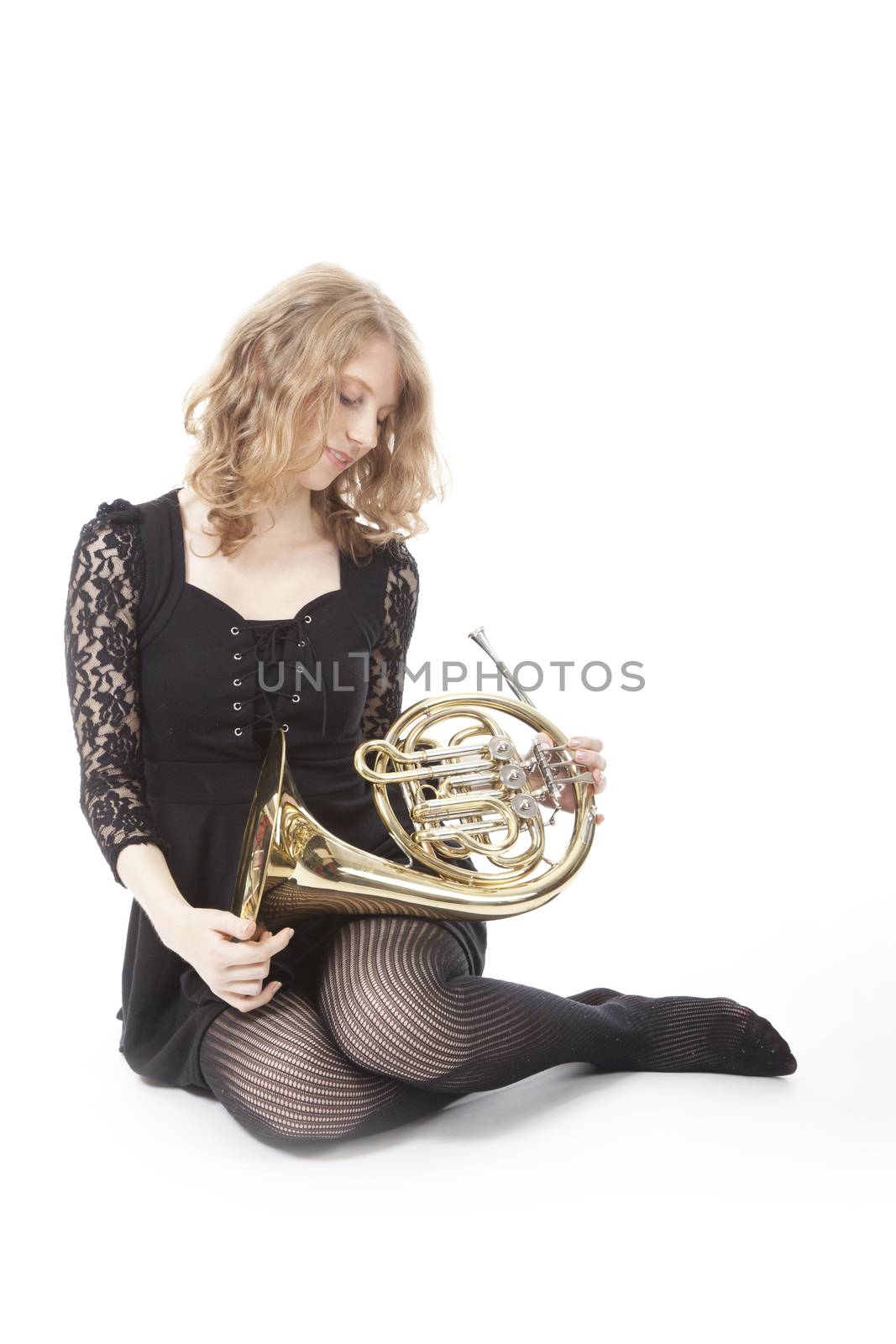 young pretty woman sitting and holding french horn against white background