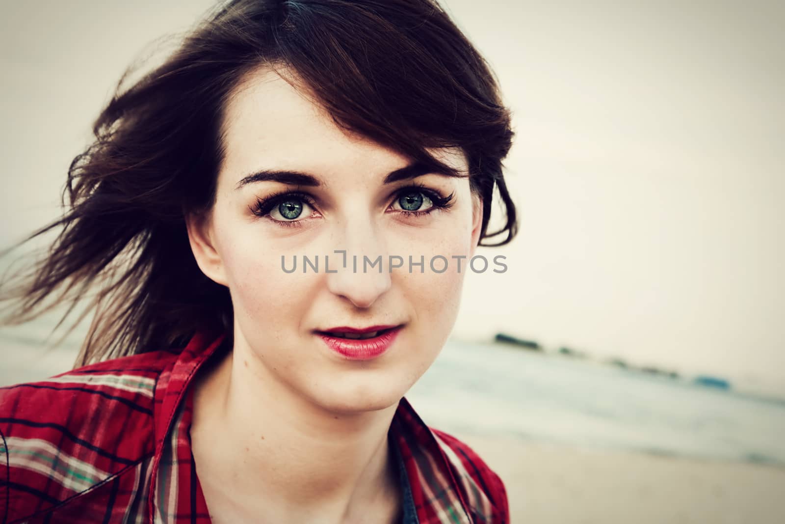 Portrait of a pretty fashionable, young woman in a chequered red shirt on the beach