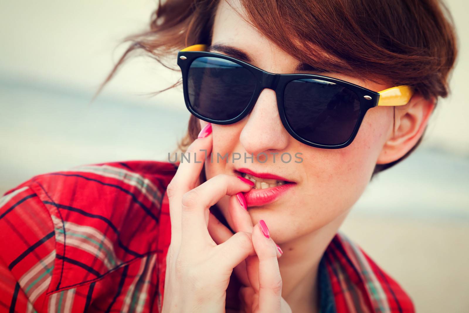 Portrait of a pretty fashionable, young woman in a chequered red shirt and sunglasses on the beach