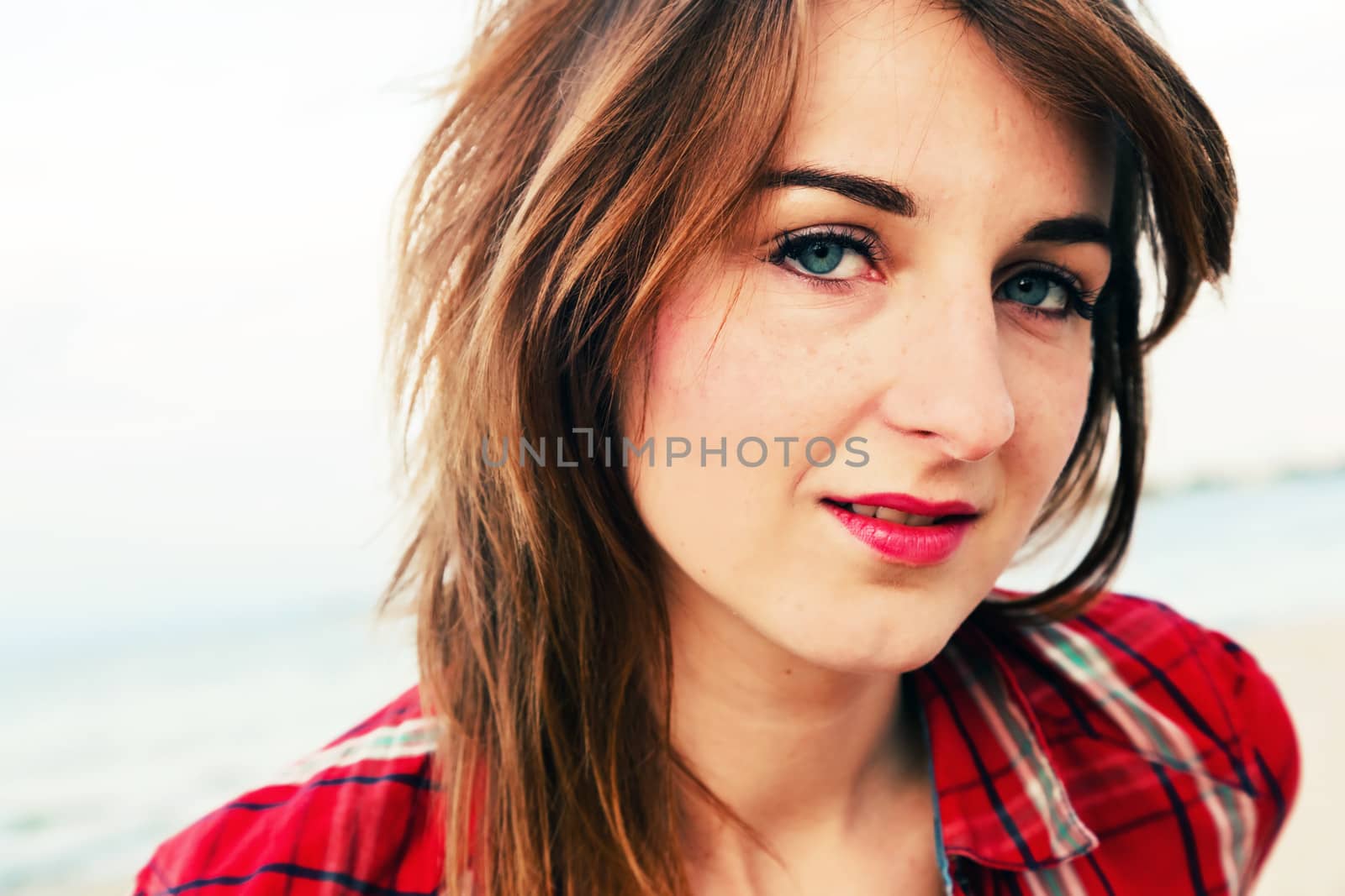 Portrait of a pretty fashionable, young woman in a chequered red shirt on the beach