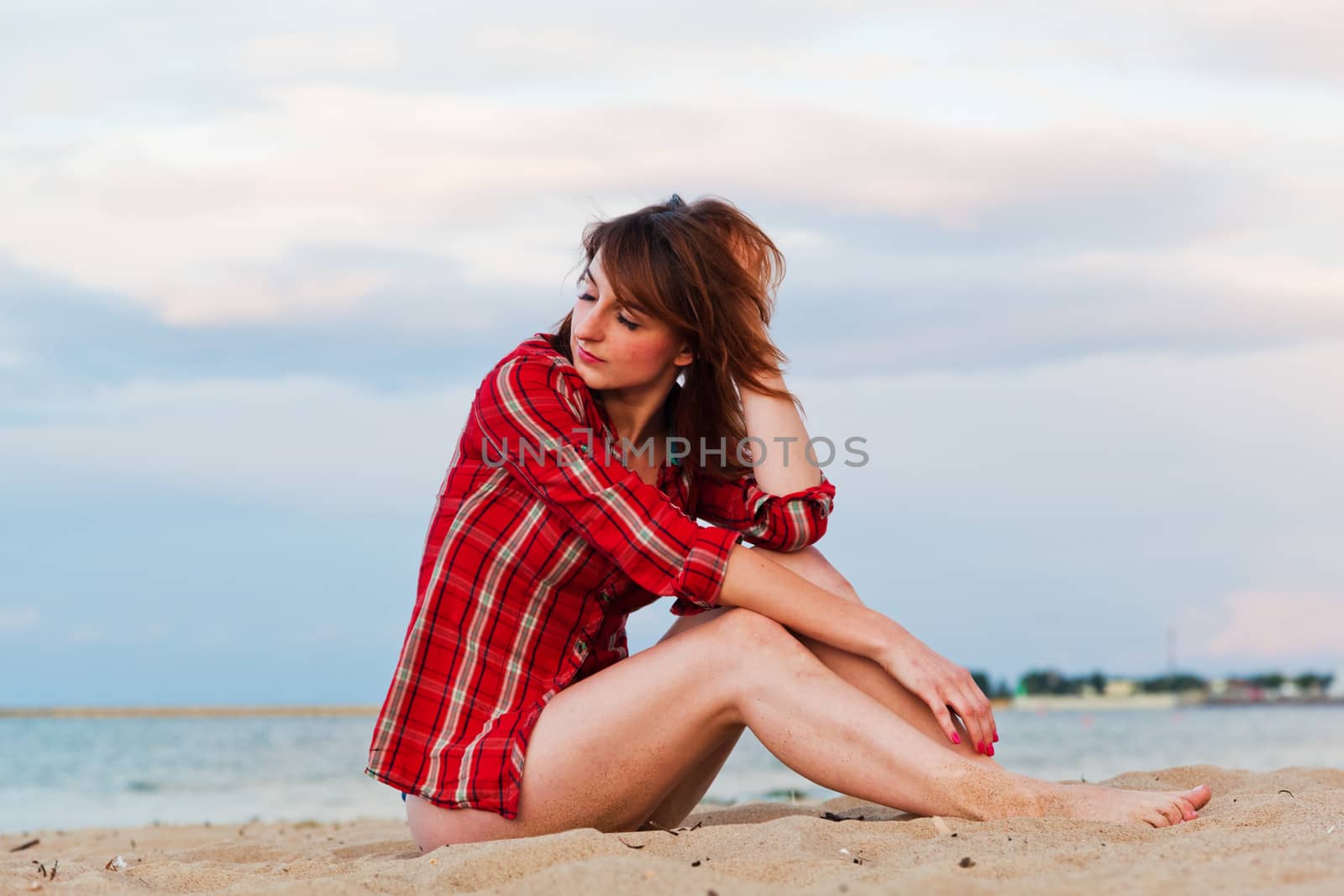 Pretty fashionable young woman in a chequered red shirt relaxing on the beach