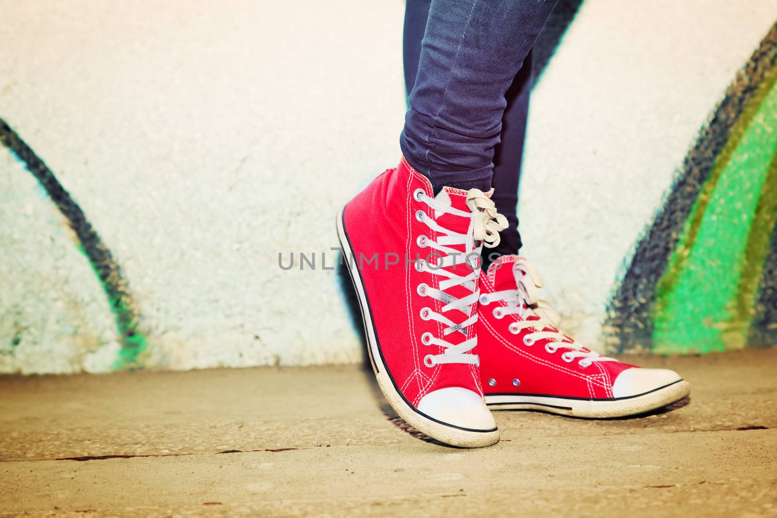 Close up of red sneakers worn by a teenager. Grunge graffiti wall