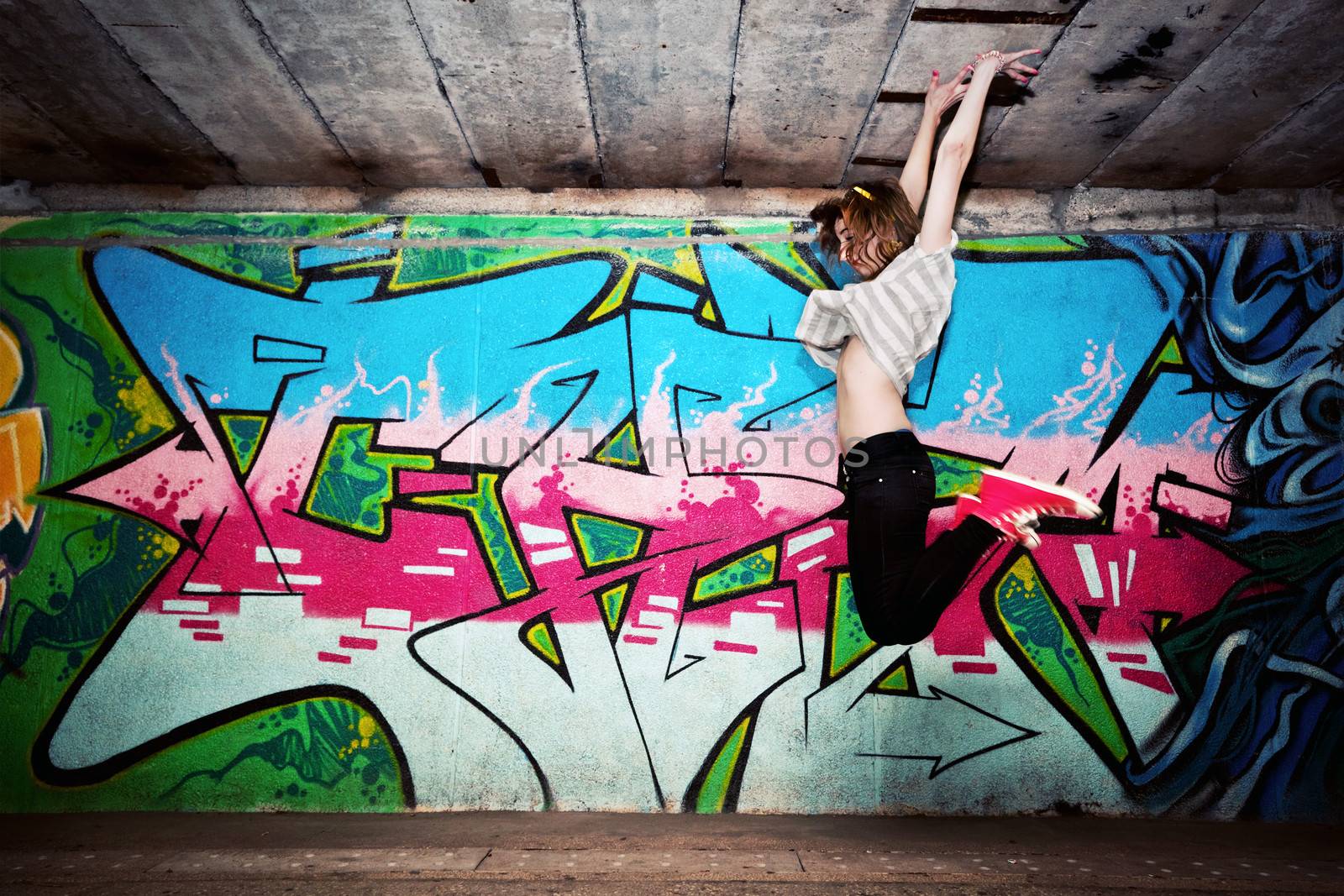 Stylish fashionable girl in a dance pose, jumping against colorful graffiti wall. Fashion, trends, subculture. Full body shot