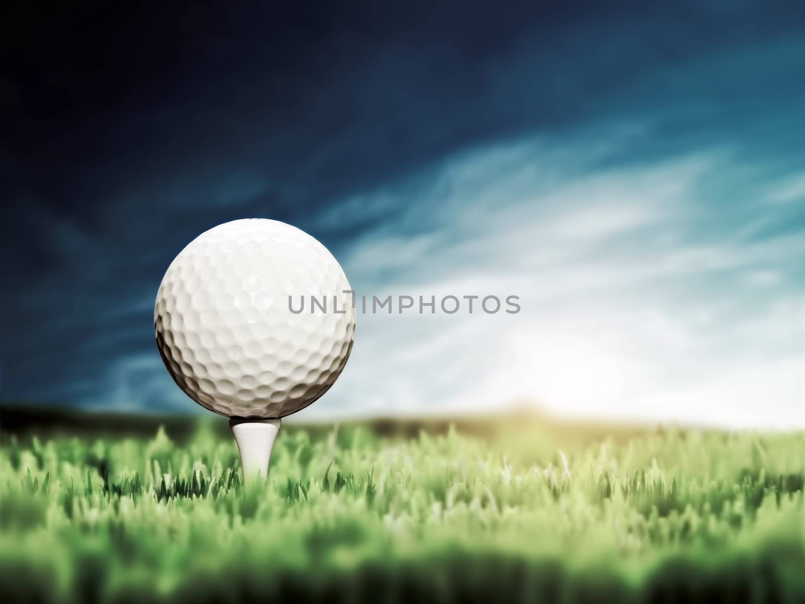 Golf ball placed on white golf tee on green grass golf course. Moody sunny sky.