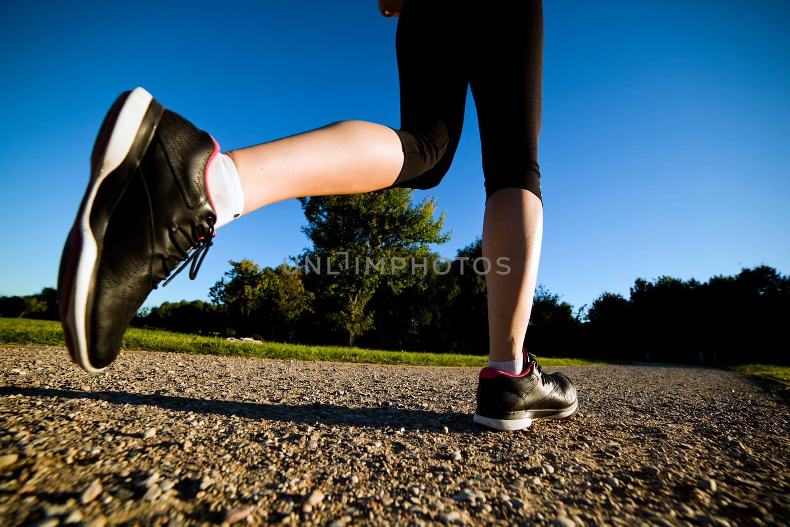 Young fit woman does running, jogging training in a park at summer sunny day. Legs close up