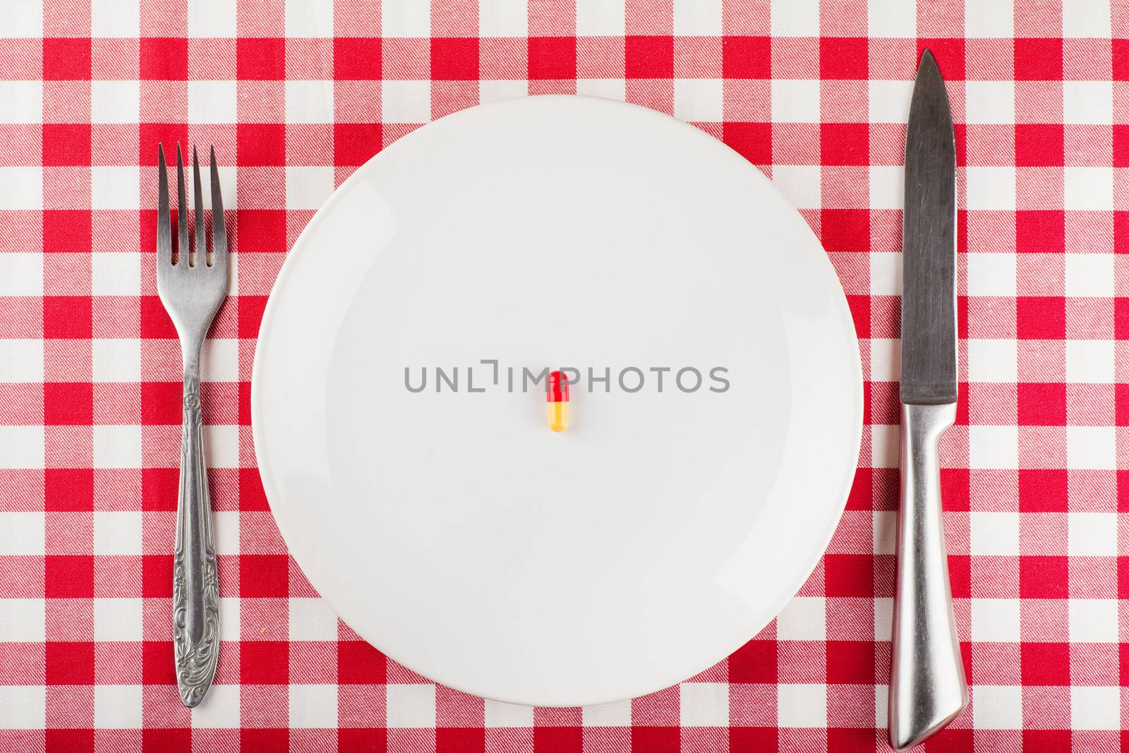 Closeup view of single capsule on a white plate with fork and knife