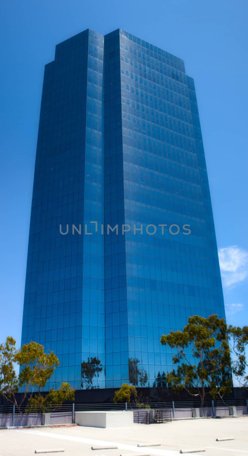 A blue mirrored skyscraper with trees in the foreground.