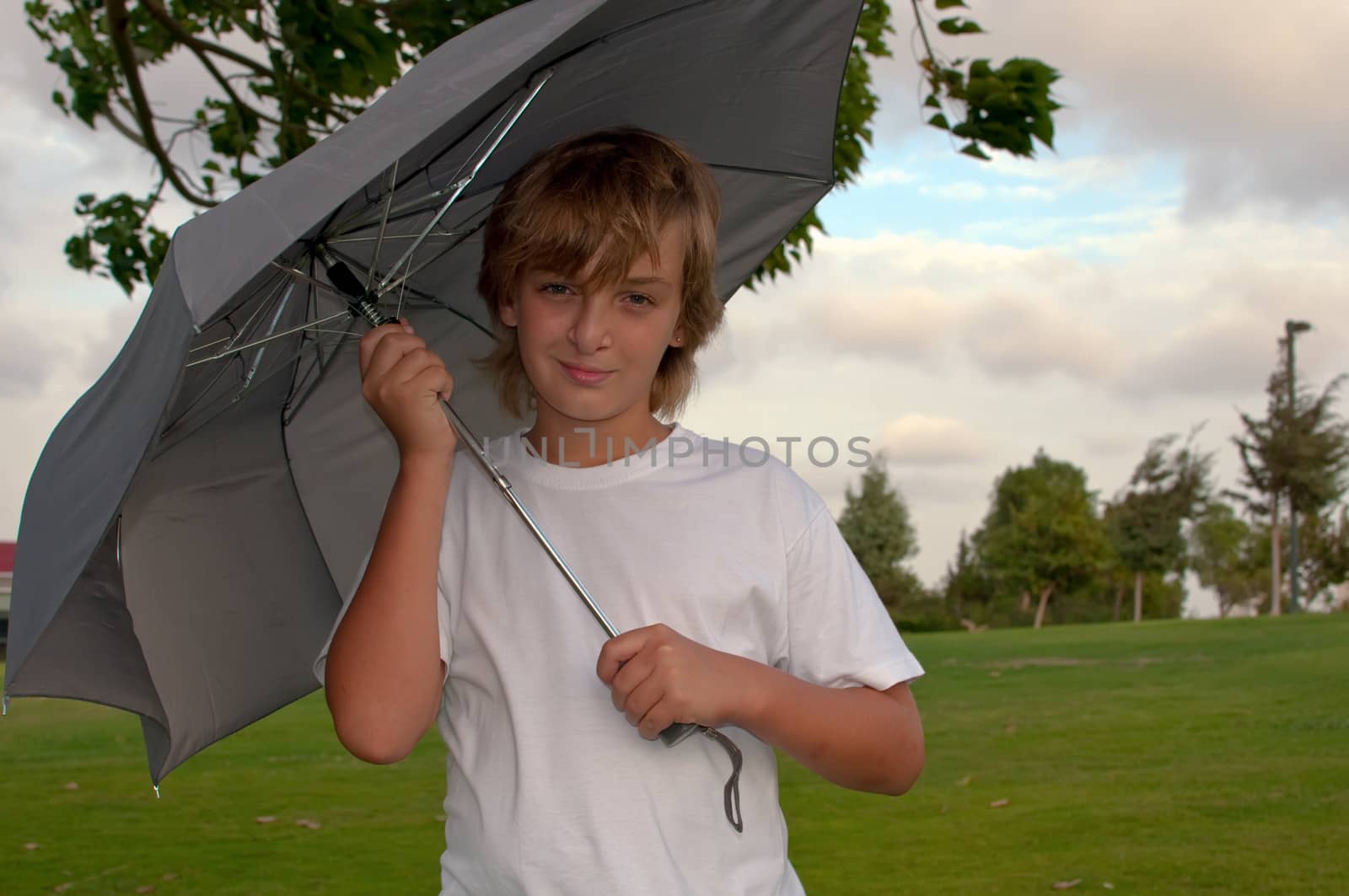 Boy looking at camera while under umbrella outside  .