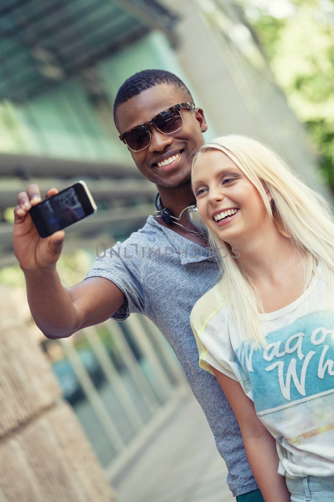 young smiling multiracial couple taking foto by smartphone outdoor in summer
