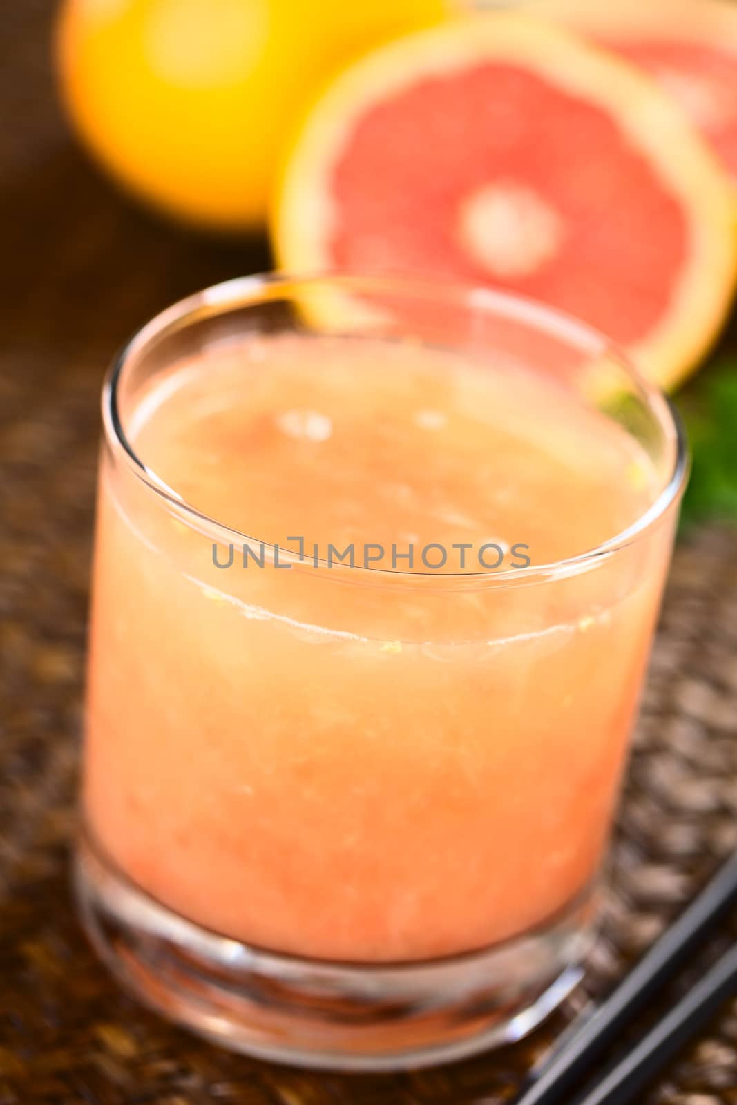 Freshly squeezed juice of the pink-fleshed grapefruit with black drinking straws on the side and grapefruits in the back (Selective Focus, Focus on the front rim of the glass)