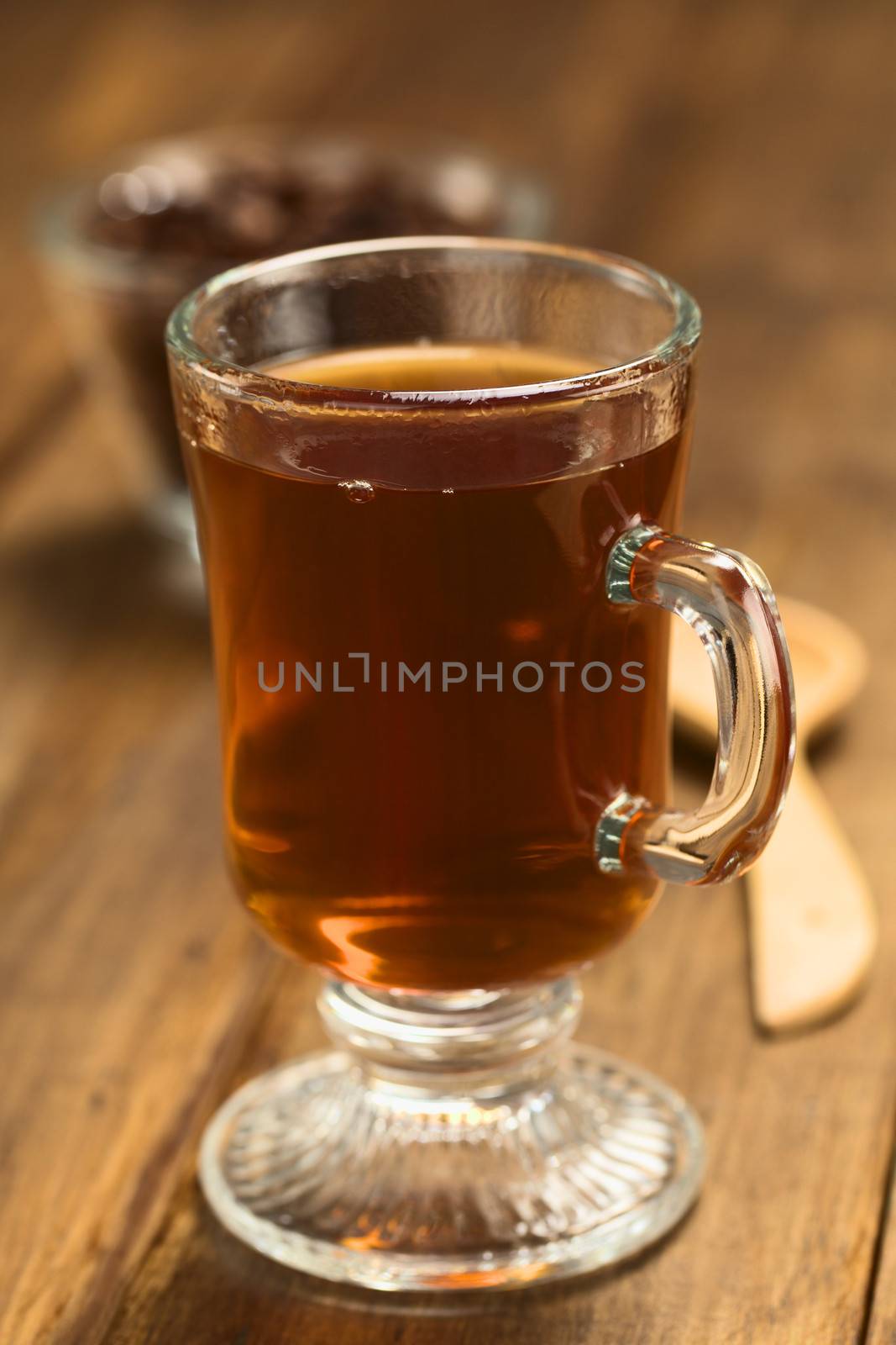 Fresh hot chocolate herbal tea made of cacao shell flakes, which is rich in flavonoids and antioxidants, served in glass on dark wood  (Selective Focus, Focus on the front of the rim of the glass)