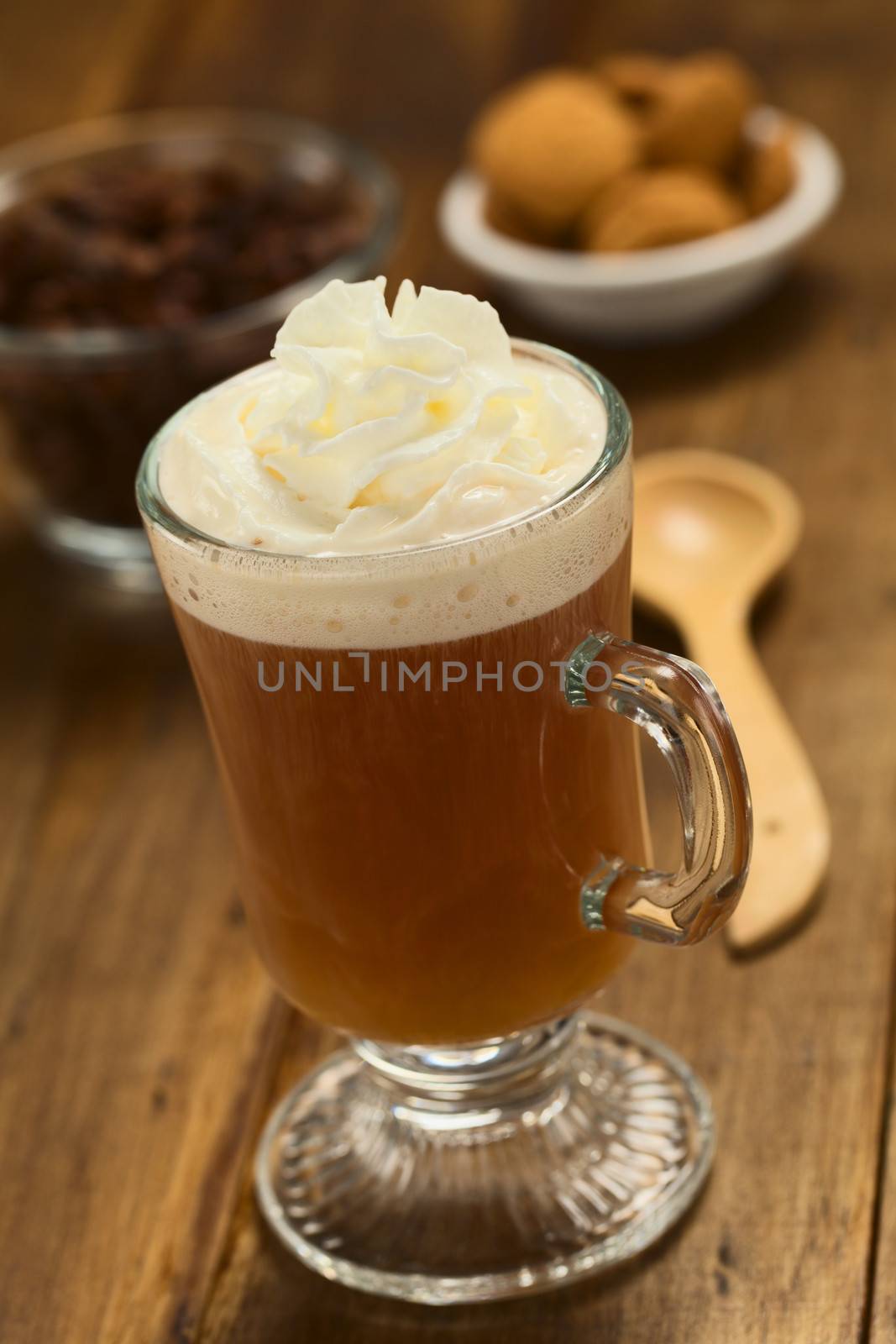 Fresh hot chocolate herbal tea made of cacao shell flakes, which is rich in flavonoids and antioxidants, served in glass with whipped cream on top on dark wood  (Selective Focus, Focus on the front of the cream)