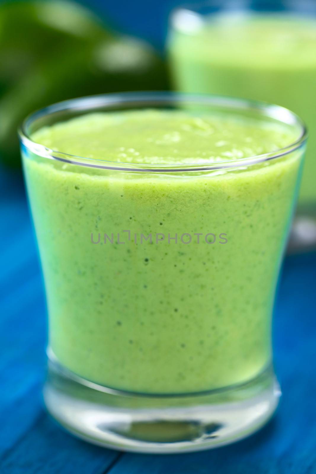 Healthy refreshing green smoothie made of fresh avocado, lime and yoghurt in glass on blue wood (Selective Focus, Focus on the front of the glass rim)