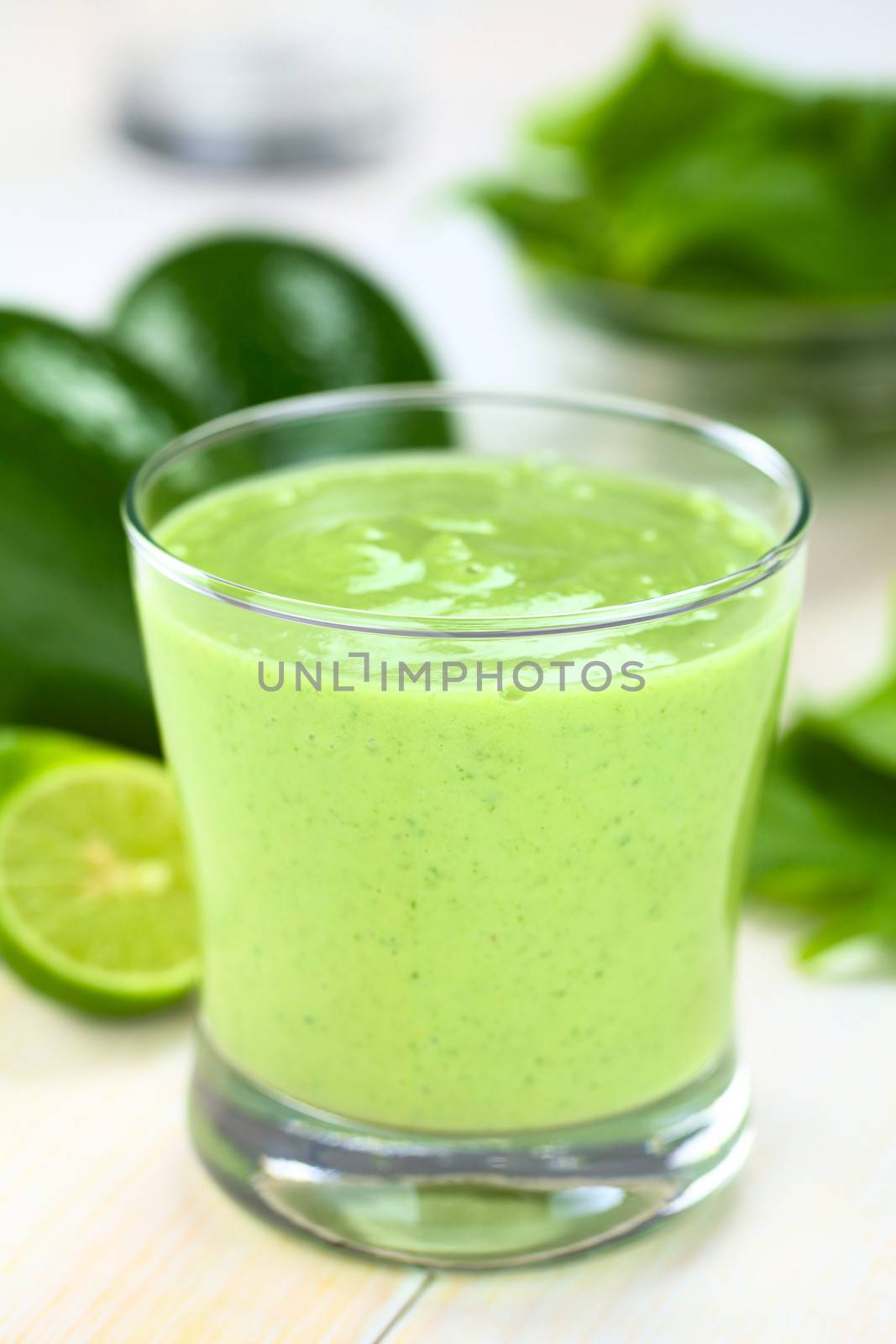 Healthy refreshing green smoothie made of fresh avocado, spinach, lime and yoghurt in a glass on bright wood (Selective Focus, Focus on the front of the glass rim)