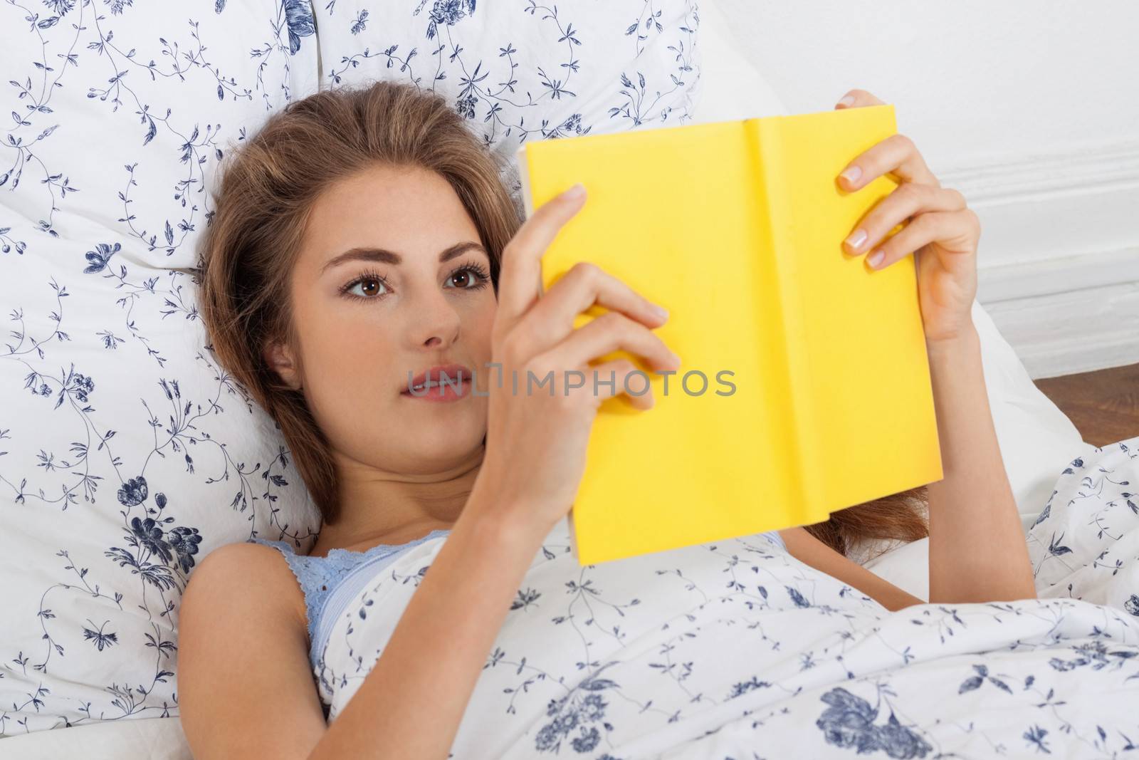 young attractive woman reading book lying in bed by juniart